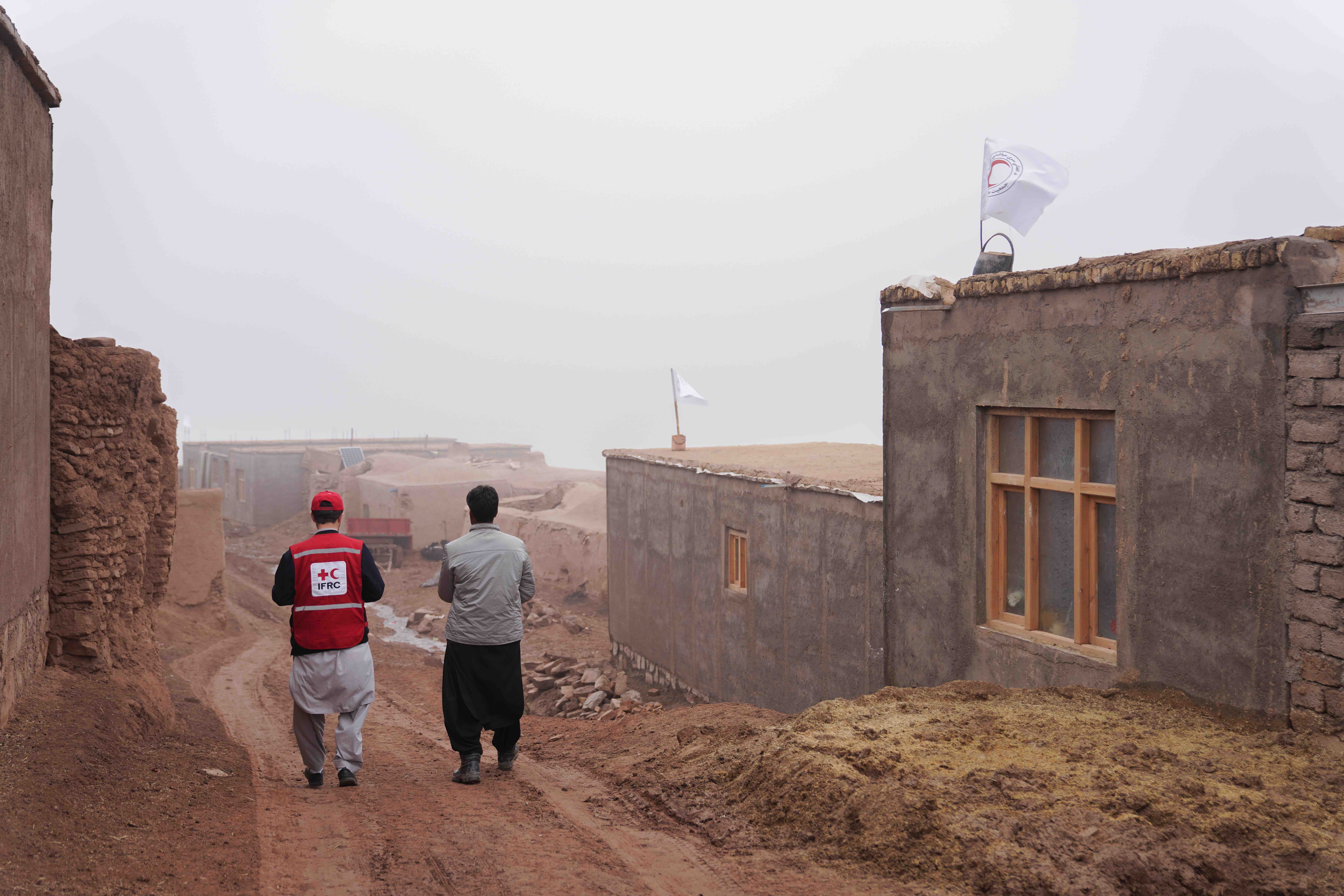 An IFRC staff member walks with a local resident among new homes built by the IFRC, the Afghan Red Crescent and other partners in the wake of devastating earthquakes in October 2023.