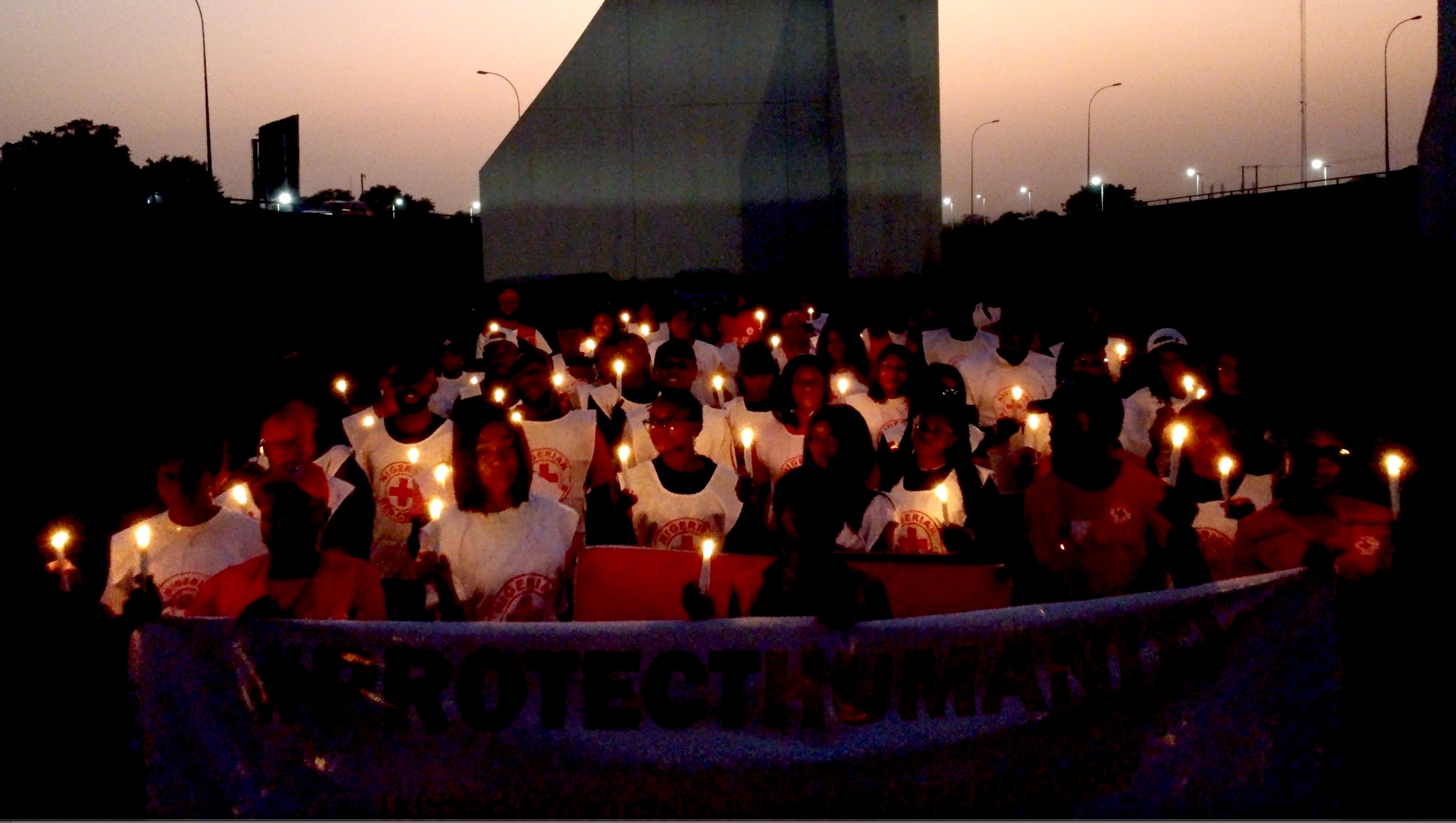 As evening fell, volunteers with the Nigerian Red Cross held candles and a large banner that read ‘Protect Humanity.’