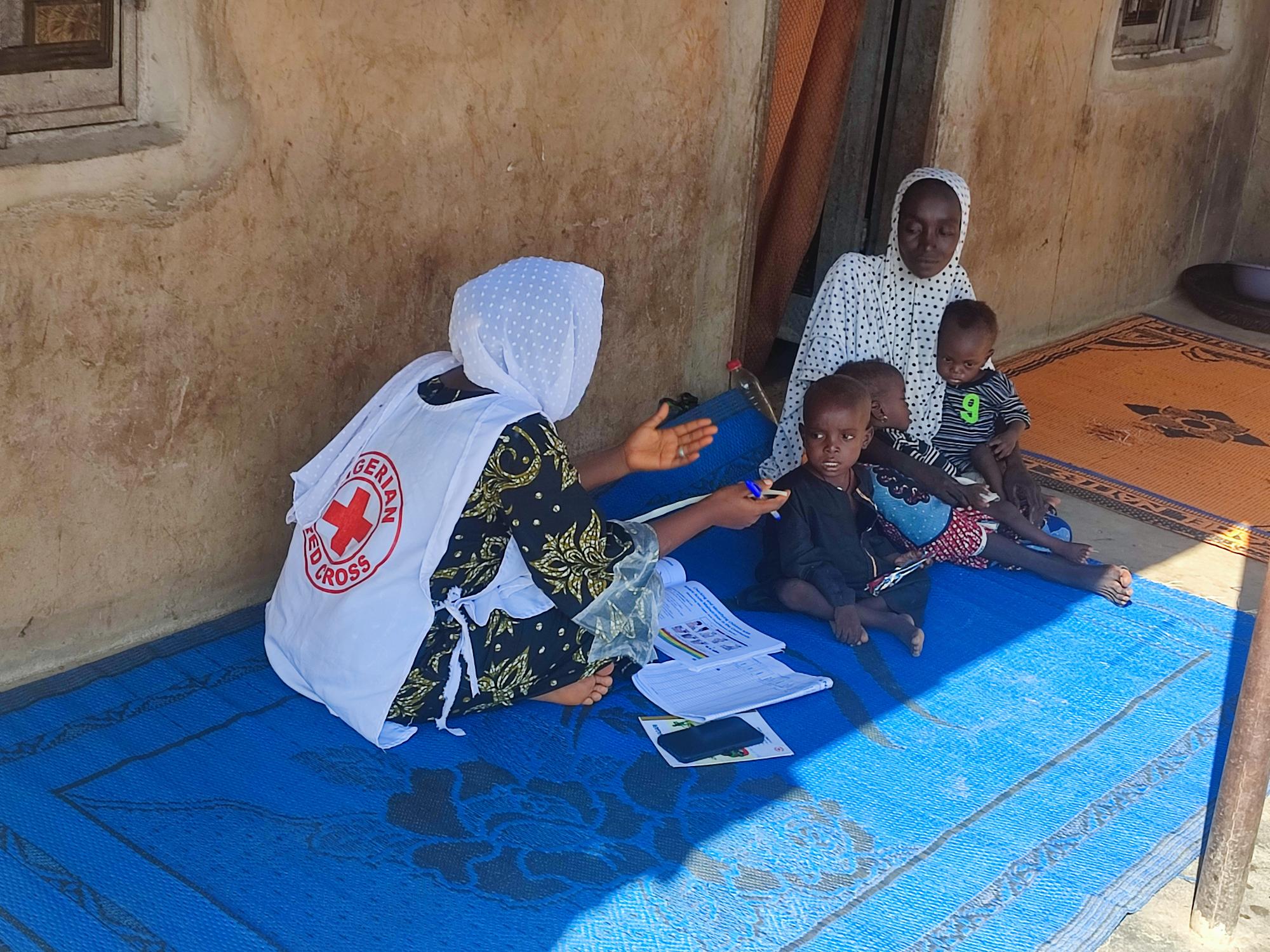A Nigerian Red Cross volunteer visits Aisha and her children in her home, checking on the helalh of her children since they began practicing handwashing.