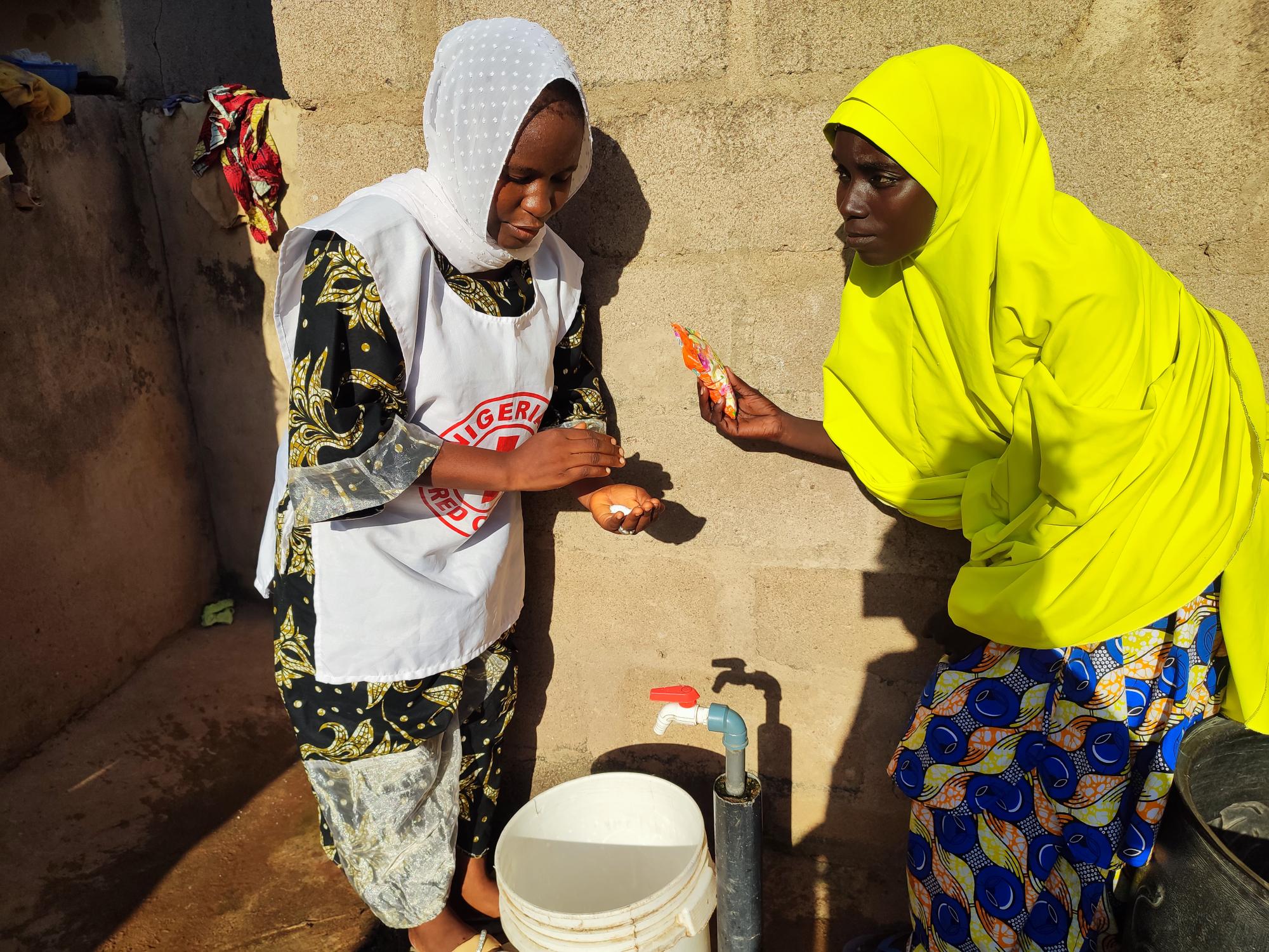 A Nigerian Red Cross volunteer shows a woman in Adamawa state, Nigeria, how to properly wash hands in order to prevent transmission of infectious diseases.  