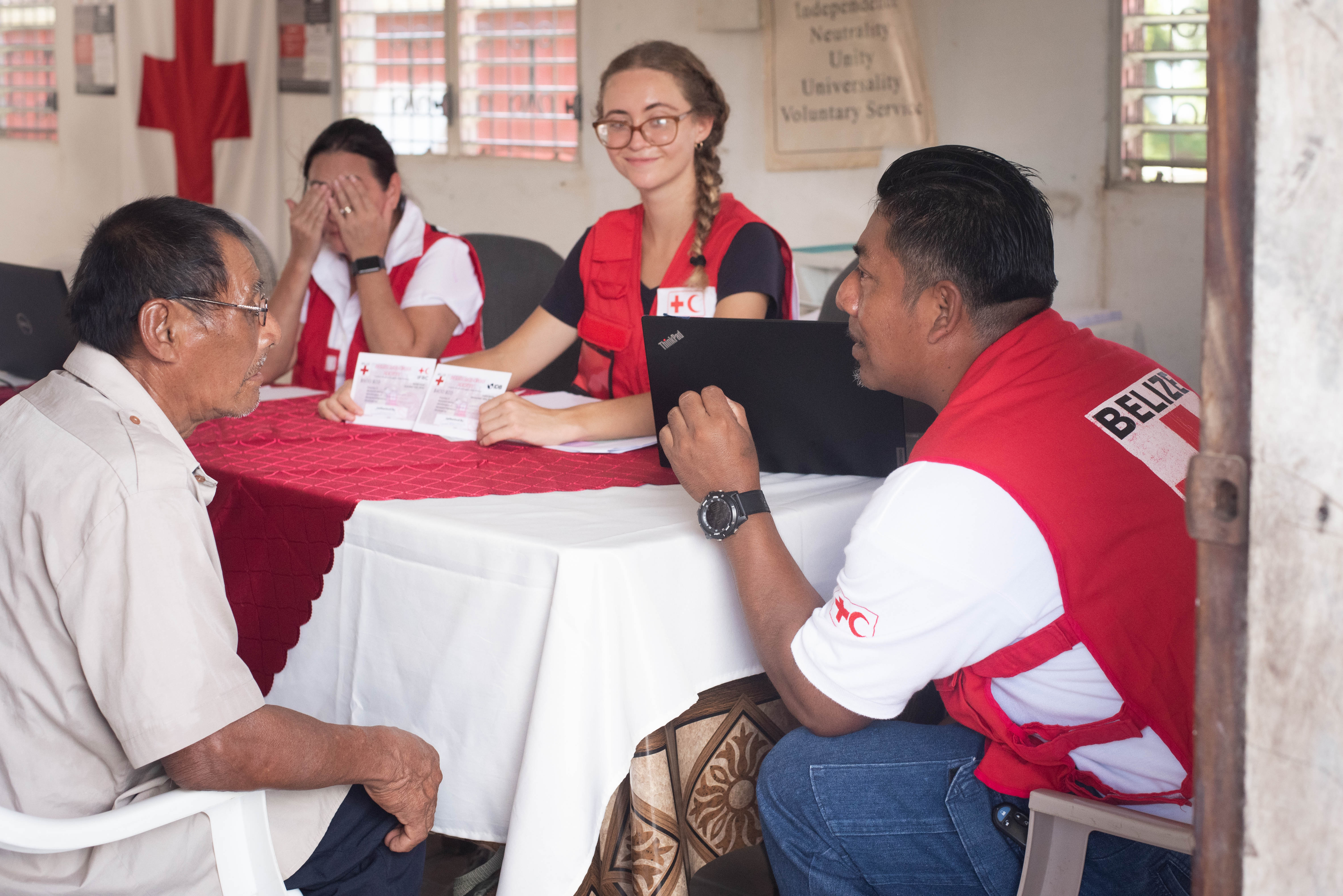 A volunteer with the Belize Red Cross’s Toledo branch, Rigoberto (right), explains to people who speak Mayan and Qʼeqchiʼ how to receive cash assistance and use vouchers to buy tools, seeds, and other implements that will help them recover their farms.  