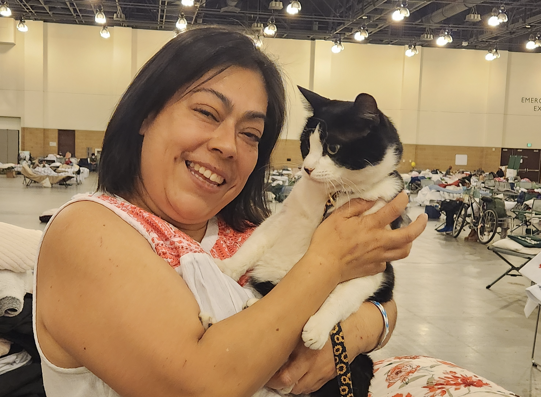 Blanca Pérez smiles and cuddles a cat inside one of the large halls being used as a temporary shelter inside the Pasadena Convention Center. Pérez lost her home and her dress shop to the fires, but she finds some comfort in the compassion and support shown by Red Cross volunteers. 