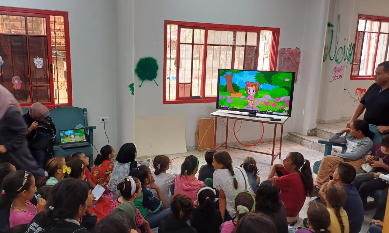 يتجمع الأطفال في جلسة نظمها الهلال الأحمر الفلسطيني لإدخال البهجة والفرح على قلوبهم وسط الضغوط النفسية التي يعانون منها بسبب النزاع. لقد كان لتأثير النزوح، والمشقة الجسدية، والخوف المستمر، عواقب وخيمة على صحتهم النفسية. 