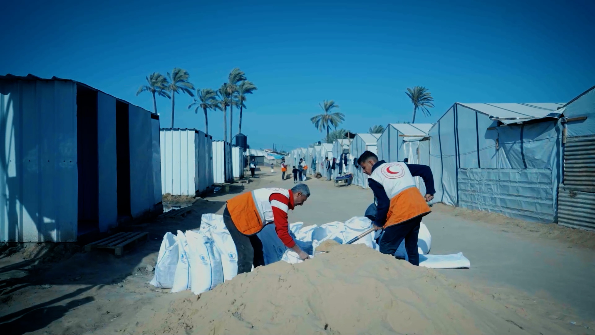 متطوعو الهلال الأحمر الفلسطيني يملؤون أكياسًا بالرمل في مخيم للنازحين في الزوايدة، وذلك كجزء من الجهود المبذولة لحماية المخيم من الفيضانات الناجمة عن الأمطار الأخيرة. 