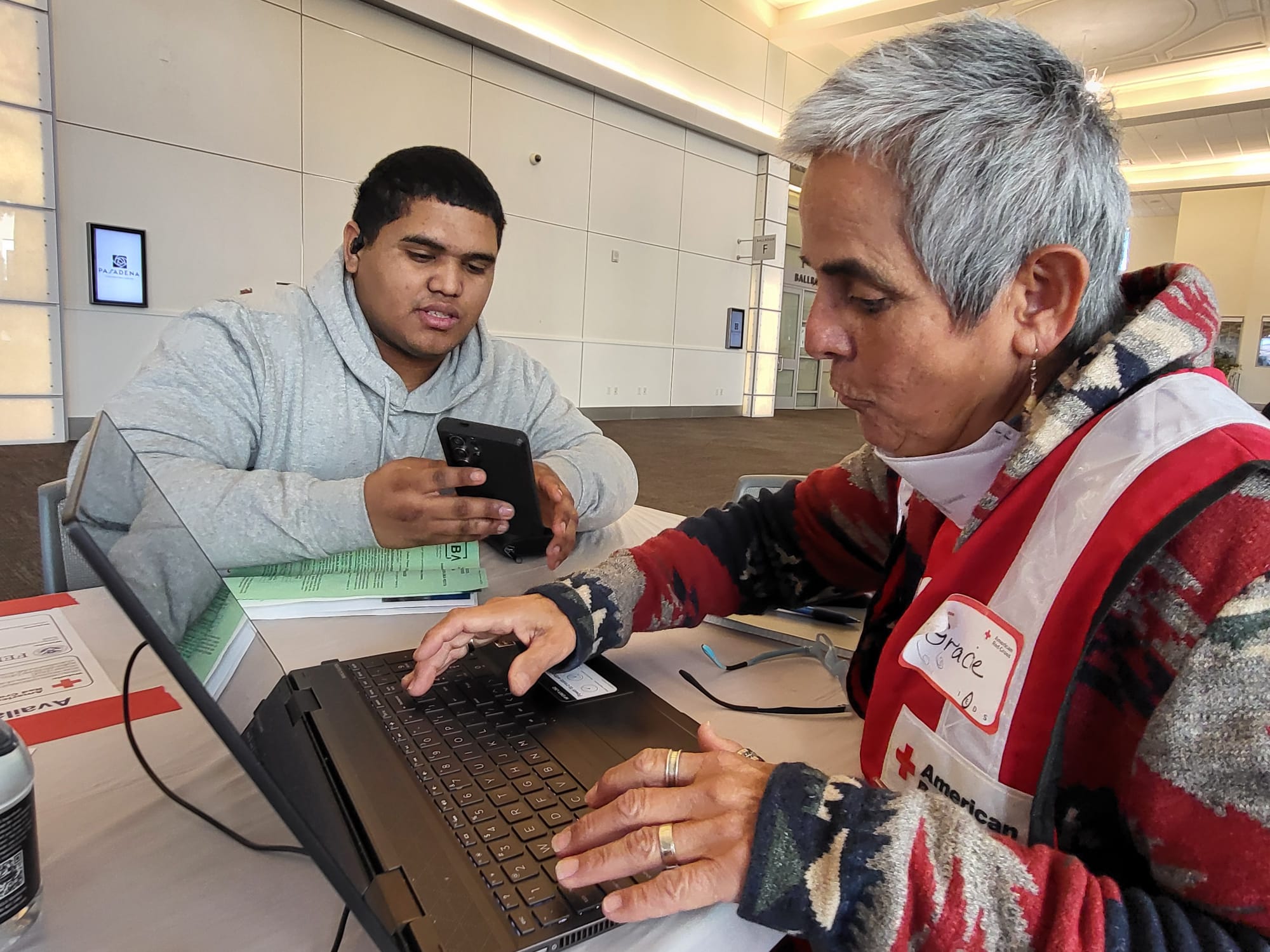 At a temporary shelter for wildfire survivors in Pasadena, California, Kennis Eduardo Díaz gets help from American Red Cross volunteer Gracie Castro, who is part of a team that helps evacuees tackle administrative tasks, find financial assistance and get referrals to services that help homeowners and renters find longer-term housing solutions.