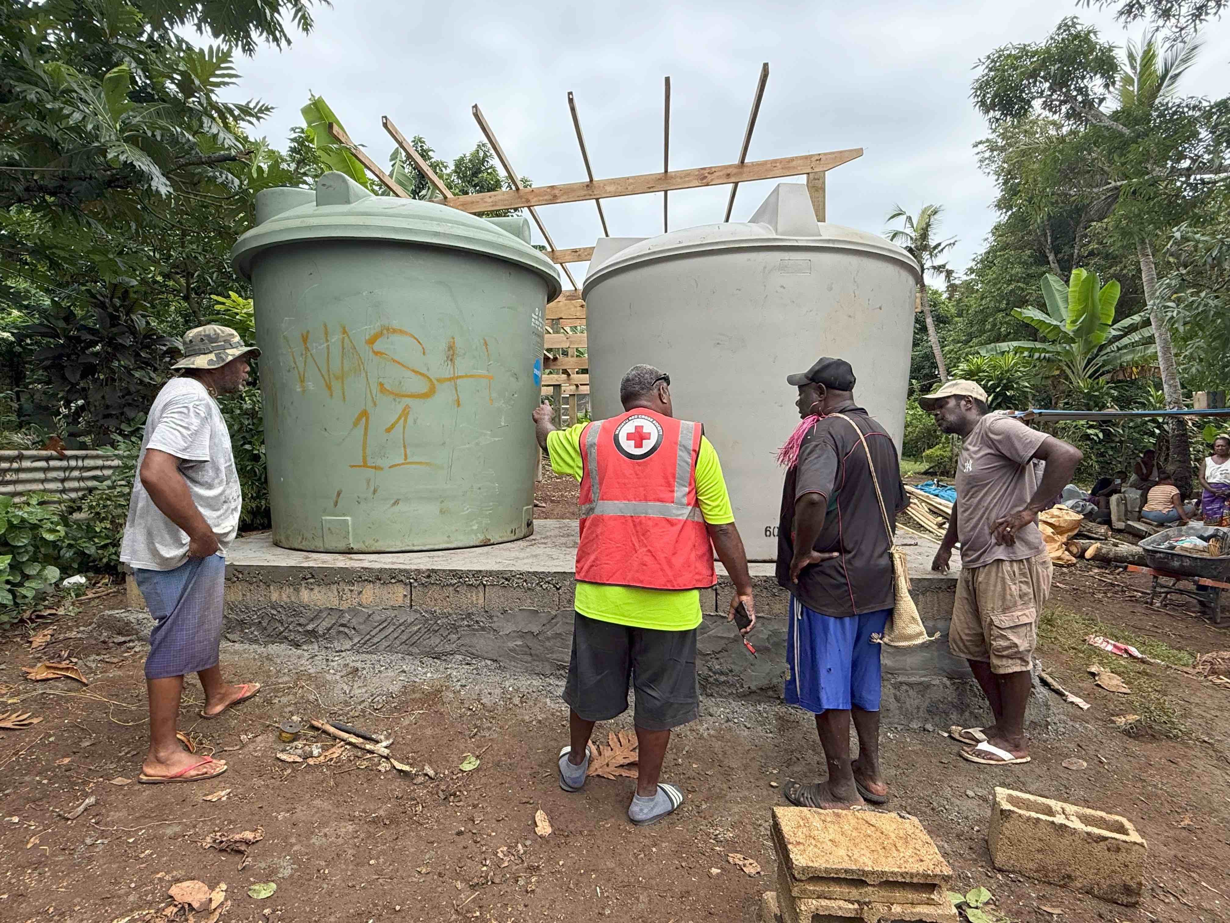 Vanuatu Red Cross water and sanitation specialists working with members of the Britano community to install two, 6000-litre water tanks that will hold rainwater gathered from the roof built above the tanks.