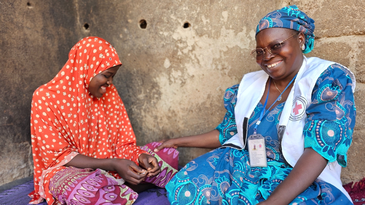 Cameroon Red Cross volunteer Rouyatou Ndjidda (right) smiles as she sits and talks with a young woman in Maroua, Far North Cameroon who recovered from catching cholera in November 2024.