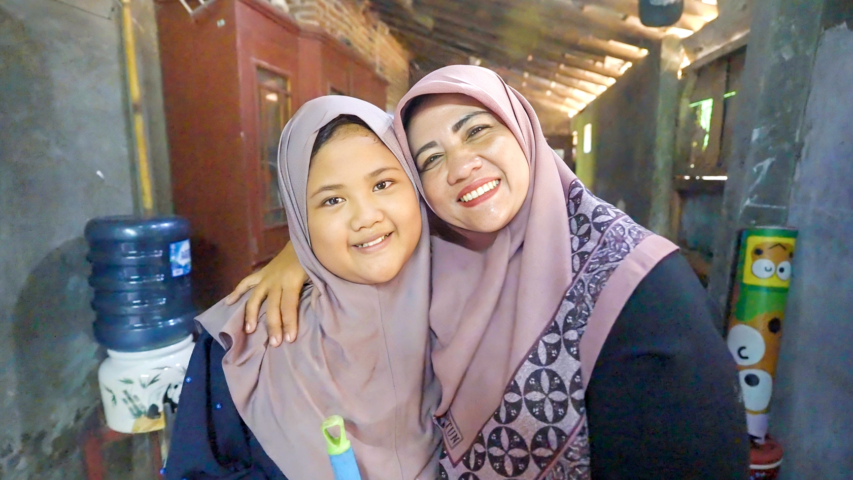10-year-old Syera (left) and her mother Evi (right) smile and hug each other in their home in Saruni village, Pandeglang, Indonesia, after Syera recovered from contracting severe dengue in February 2024.