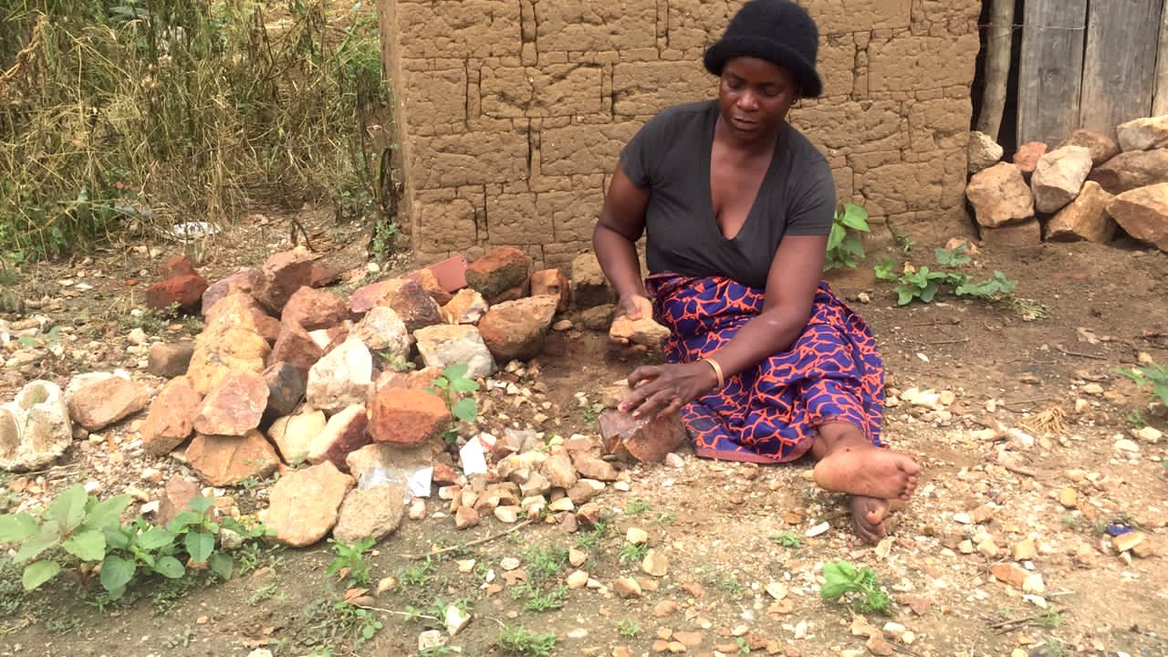 Sitting on the ground near her home, 49-year-old Patricia crushes stones that are then sold to people for use in building projects. This is one of several ways she supports her family. 
