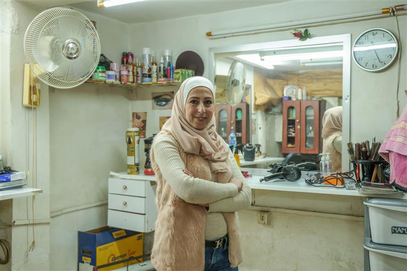 تبتسم رانيا وهي تقف داخل صالون تصفيف الشعر الخاص بها، والذي أصبح الآن مزدهراً بفضل الدعم الذي قدمه الهلال الأحمر العربي السوري. 