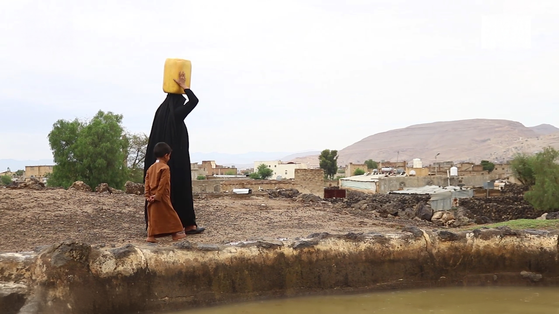 A woman carries a plastic jug full of water on her head as she walks with her son back to town. People in this Yemeni village often have to walk long distances to fetch clean water.