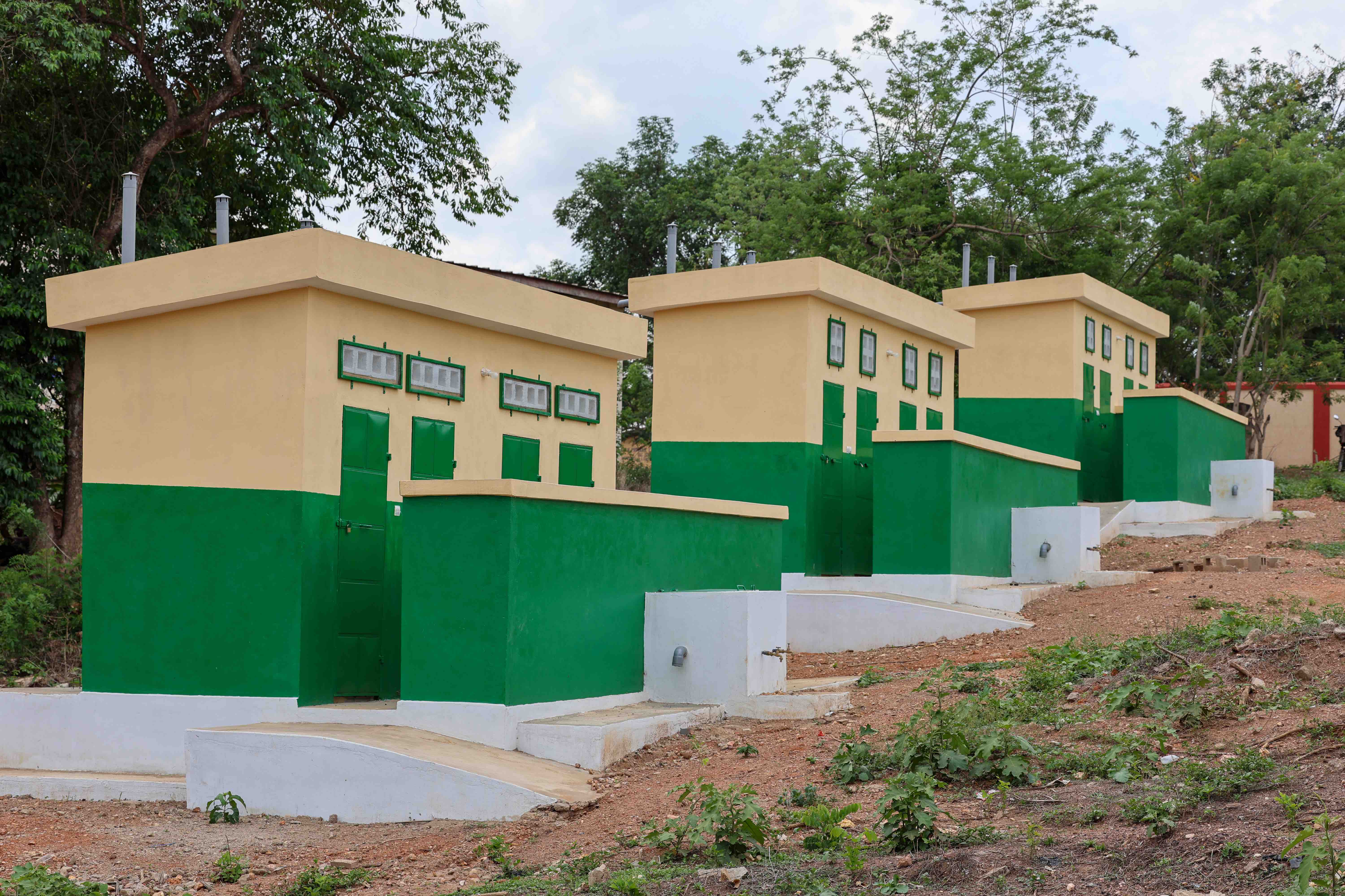 A series of three newly built latrine and water facilities, painted in bright green and beige colors, now serve a community where sanitation services had been lacking.
