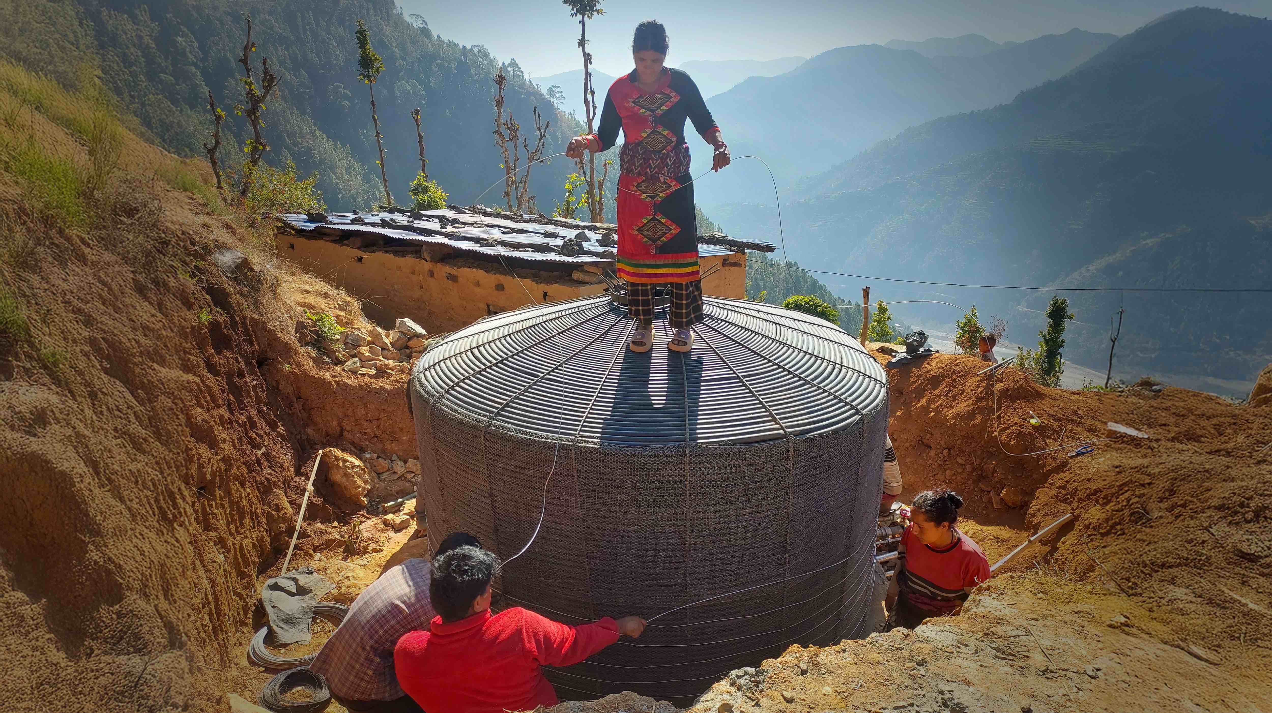 As part of a local team constructing a new water reservoir, Hajari Oli, stands atop the nearly completed water tank as she helps neighbours and Nepal Red Cross workers install the tank near her remote rural hillside community of Sanibheri, in Rukum West.  Hajari Oli also serves as treasurer of her local water-user committee.