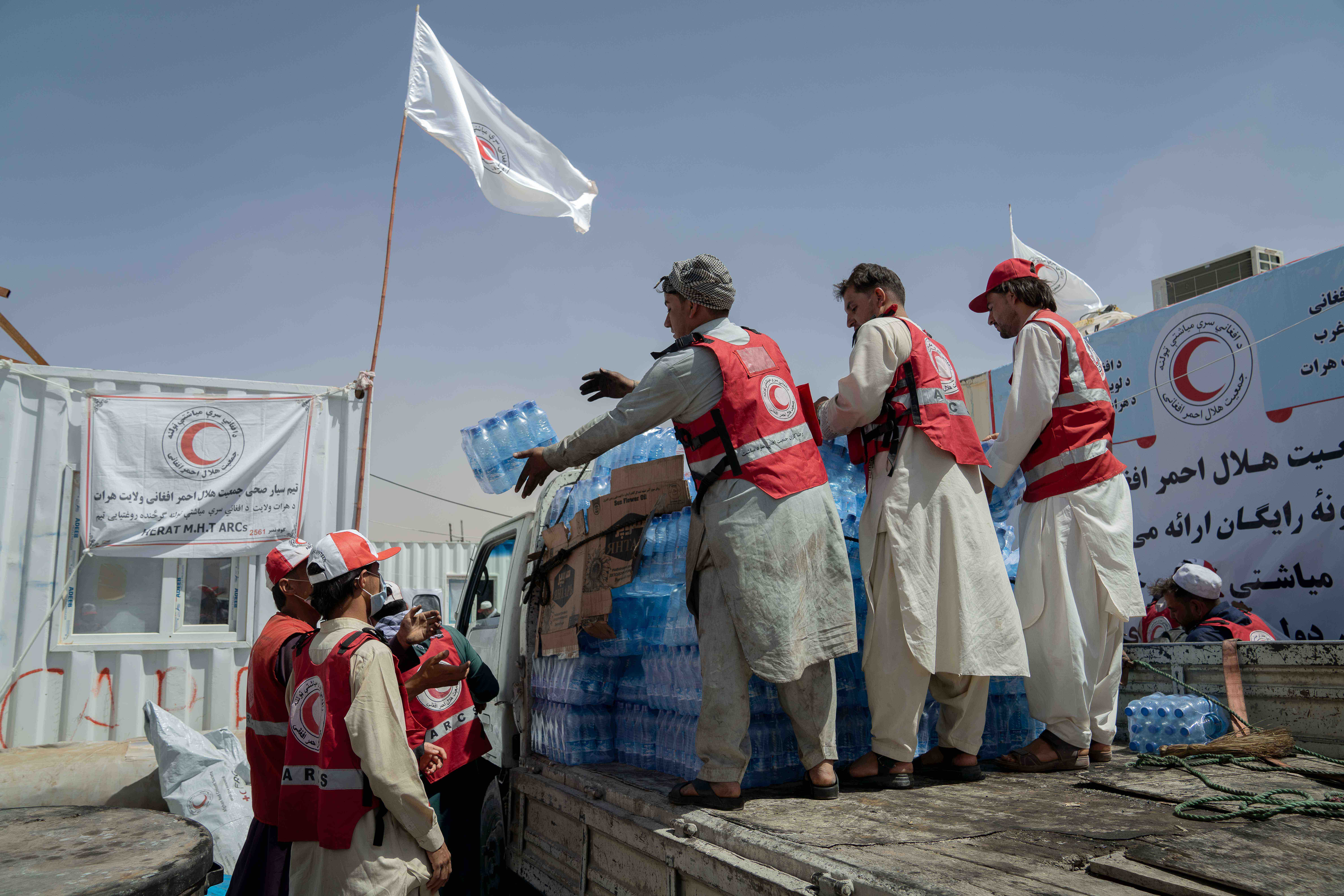 Voluntarios de la Media Luna Roja Afgana descargan botellas de agua para las personas que llegan al paso fronterizo de Islam Qala, en el oeste de Afganistán, donde las familias suelen soportar temperaturas sofocantes que a menudo superan los 40 °C.