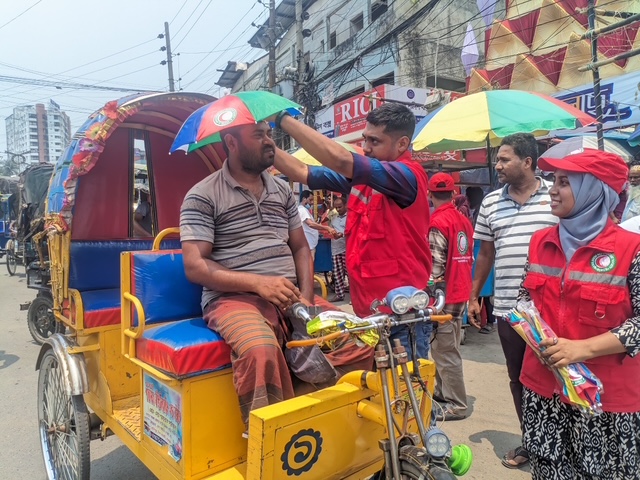 Volunteers with the Bangladesh Red Crescent Society give umbrella hats to rickshaw drivers who spend hours transporting people and goods through scorching city streets. The volunteers also provide water and information on how to avoid heat exhaustion and heat stroke.