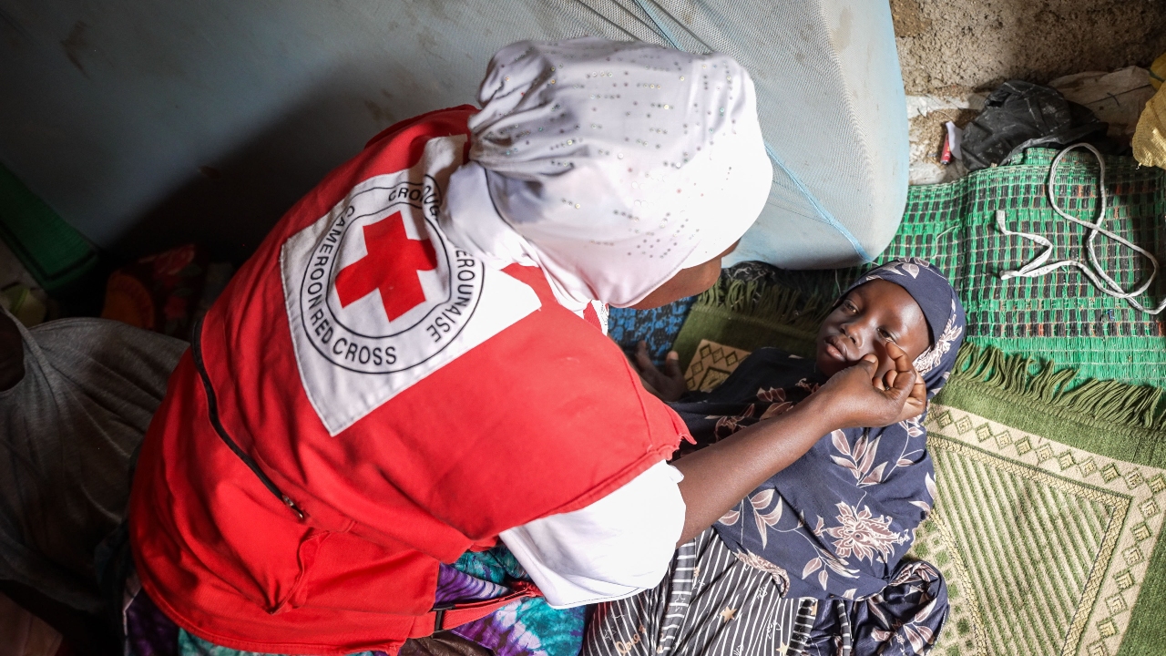 Cameroon Red Cross volunteer, Ramatou, checks Djoubeda’s eyes for redness and looks out for other signs and symptoms of measles.