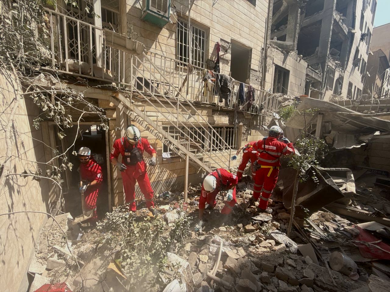 Iranian Red Crescent emergency response teams search for survivors amid the debris and rubble of buildings damaged and destroyed by recent attacks.