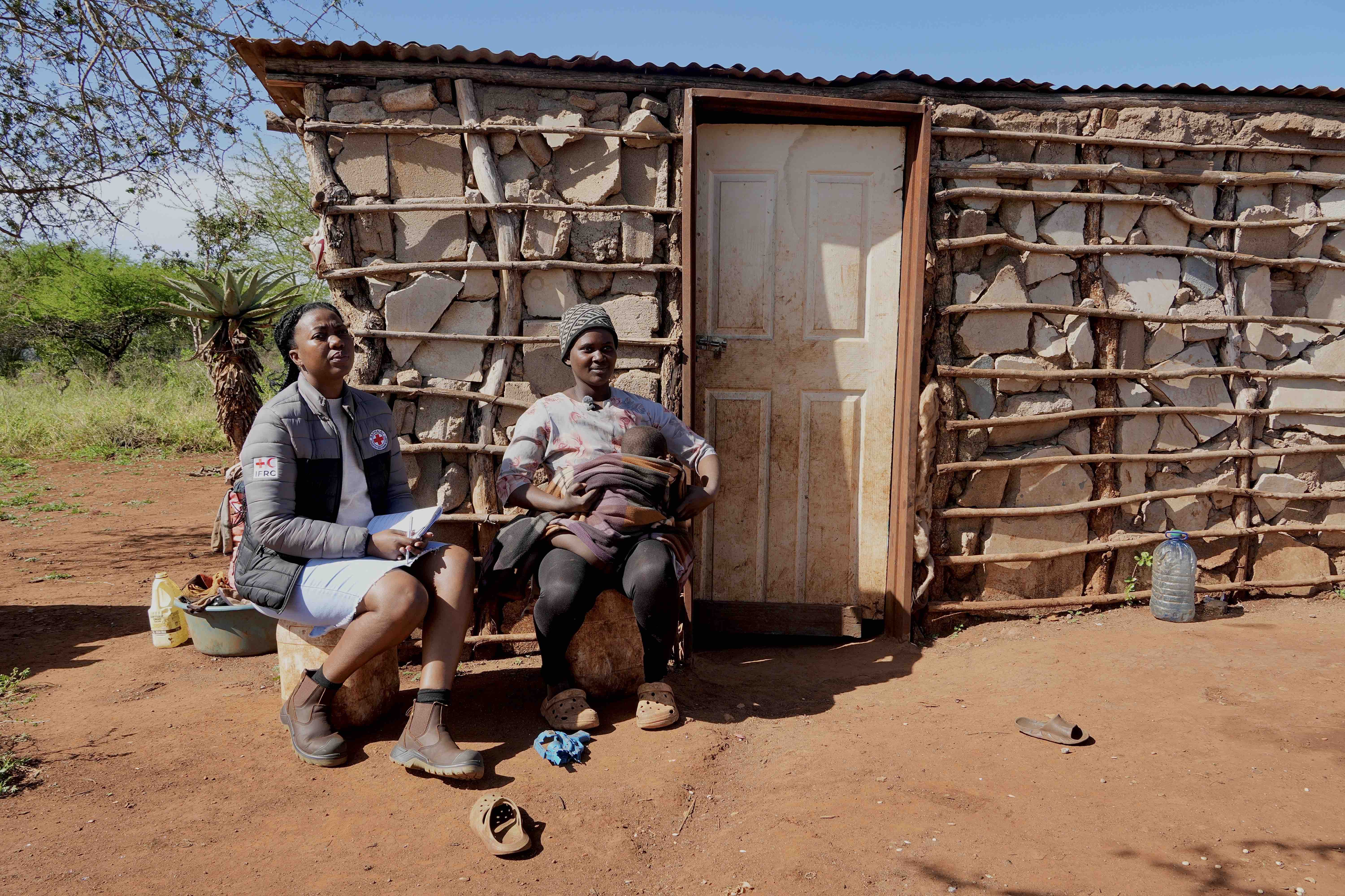 A 31-year-old mother of five, Banele Mamba holds one of her five children in front of her flood-damaged home as she talks with a member of the Baphalali Eswatini Red Cross Society. 