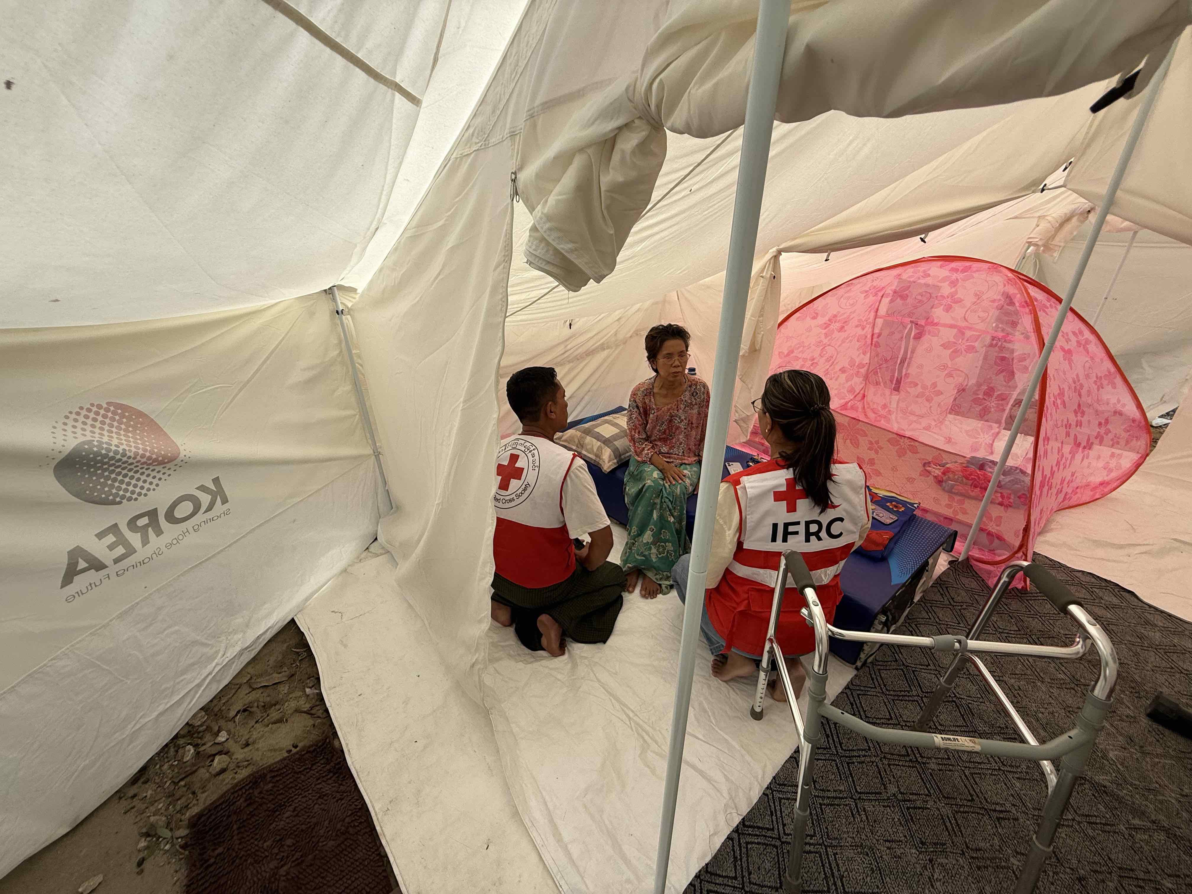 Staff members from the IFRC and the Myanmar Red Cross volunteer meet with a woman living in a tent set up by the Myanmar Red Cross.