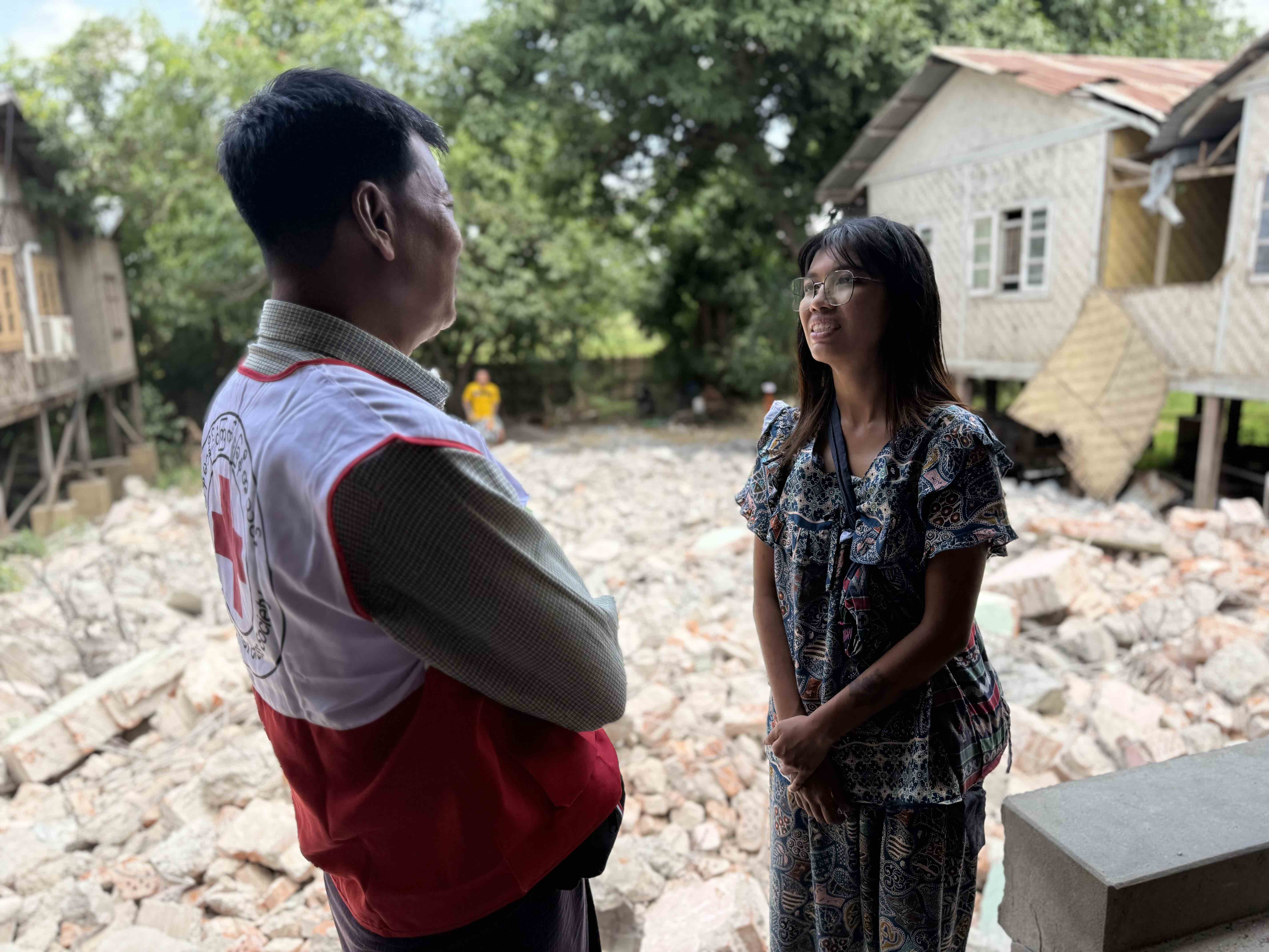 Earthquake survivor Yadanar Yu Hlaing Kyuu (right) speaks with a volunteer of the Myanmar Red Cross Society in front of an empty lot full of rubble where her house once stood.