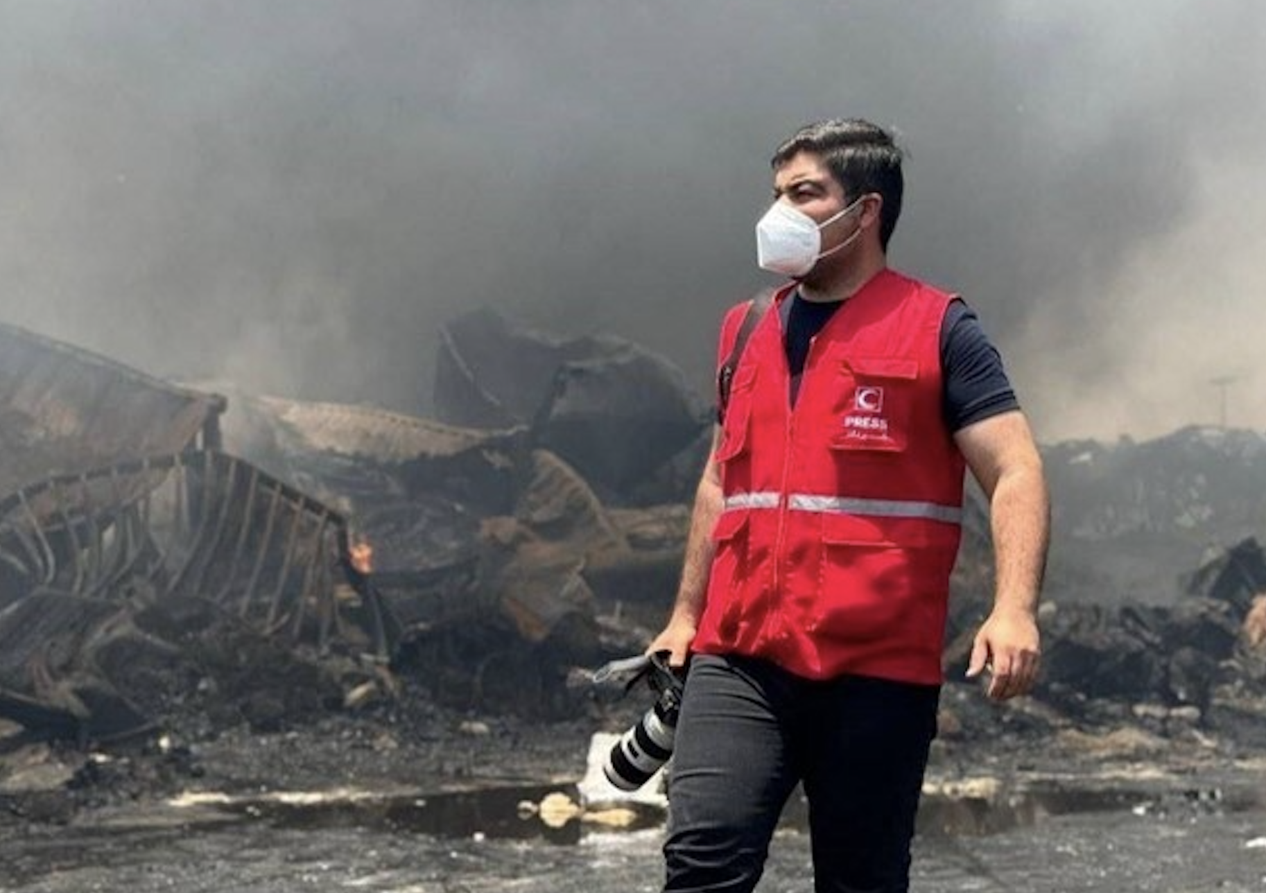 Iranian Red Crescent first responder Nima Ahmadi stands with his camera amid the still-smoldering ruins of a recently bombed building. He has served with the Iranian Red Crescent, providing first aid, saving lives and documenting humanitarian work through his camera lens.