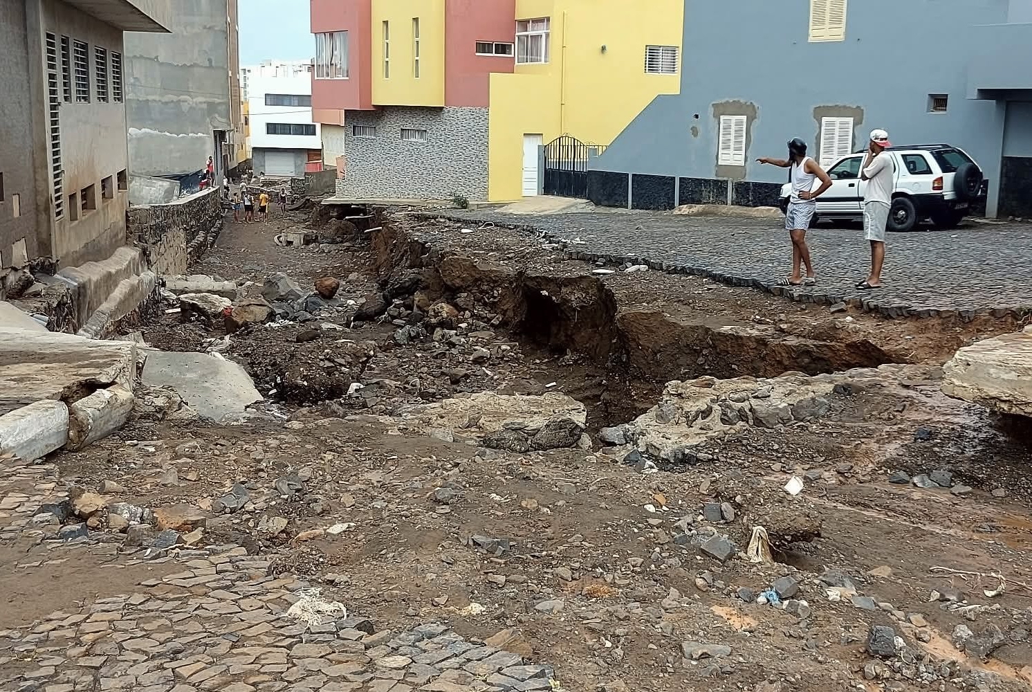 Civiles observan un pequeño cañón que antes era una concurrida calle de la ciudad. El profundo barranco, lleno de rocas, barro y escombros, fue creado por las inundaciones tras las fuertes lluvias del 10 de agosto.