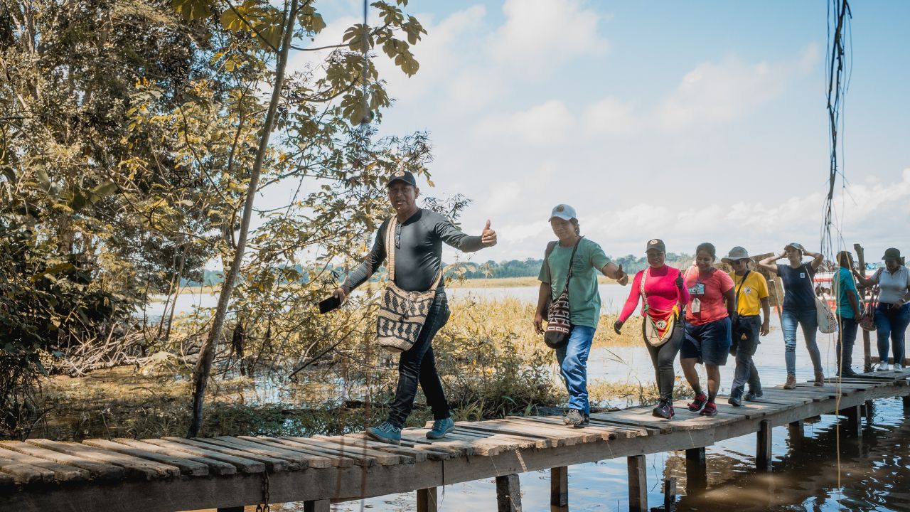 Un grupo de personas camina por el muelle que lleva a la comunidad de Mocagua, en la rivera del río Amazonas, cerca de la triple frontera entre Colombia, Perú y Brasil. Esa comunidad lidera prácticas de resiliencia climática, como la elaboración de calendarios ecológicos y sistemas de monitoreo de sequías e inundaciones.