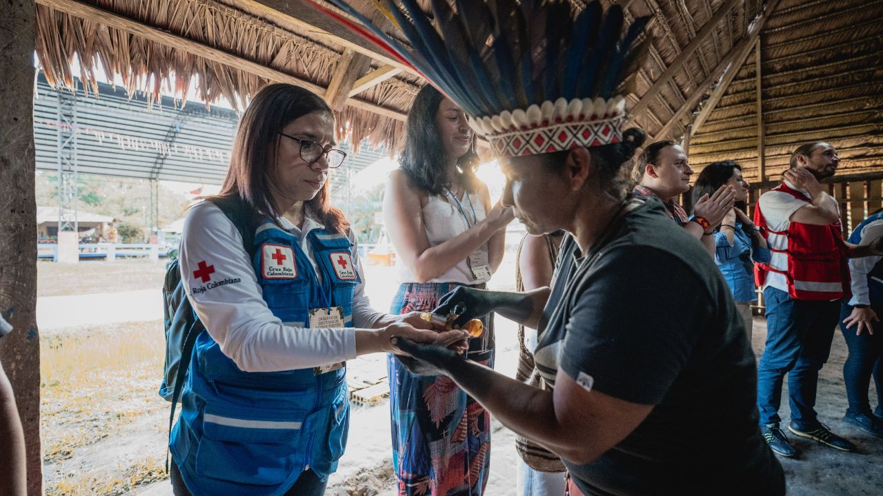 Una mujer indígena le comparte unas gotas de aceite en las manos a Marilyn Bonfante Zárate, lideresa de Cruz Roja Colombiana, durante el primer diálogo de sistemas de conocimiento sobre resiliencia climática comunitaria.