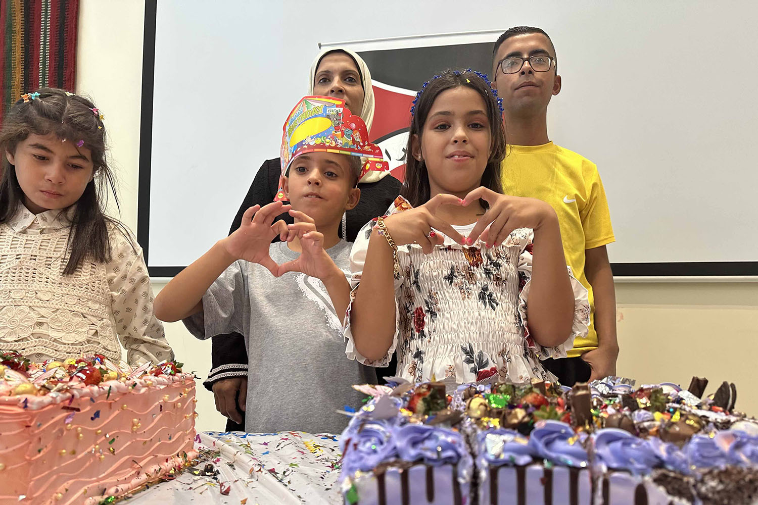 Standing in front of two birthday cakes, Alma and one of her brothers use their hands to make the sign of a heart during a birthday party organized by the Jordan Red Crescent at the hospital it runs in Amman, Jordan.
