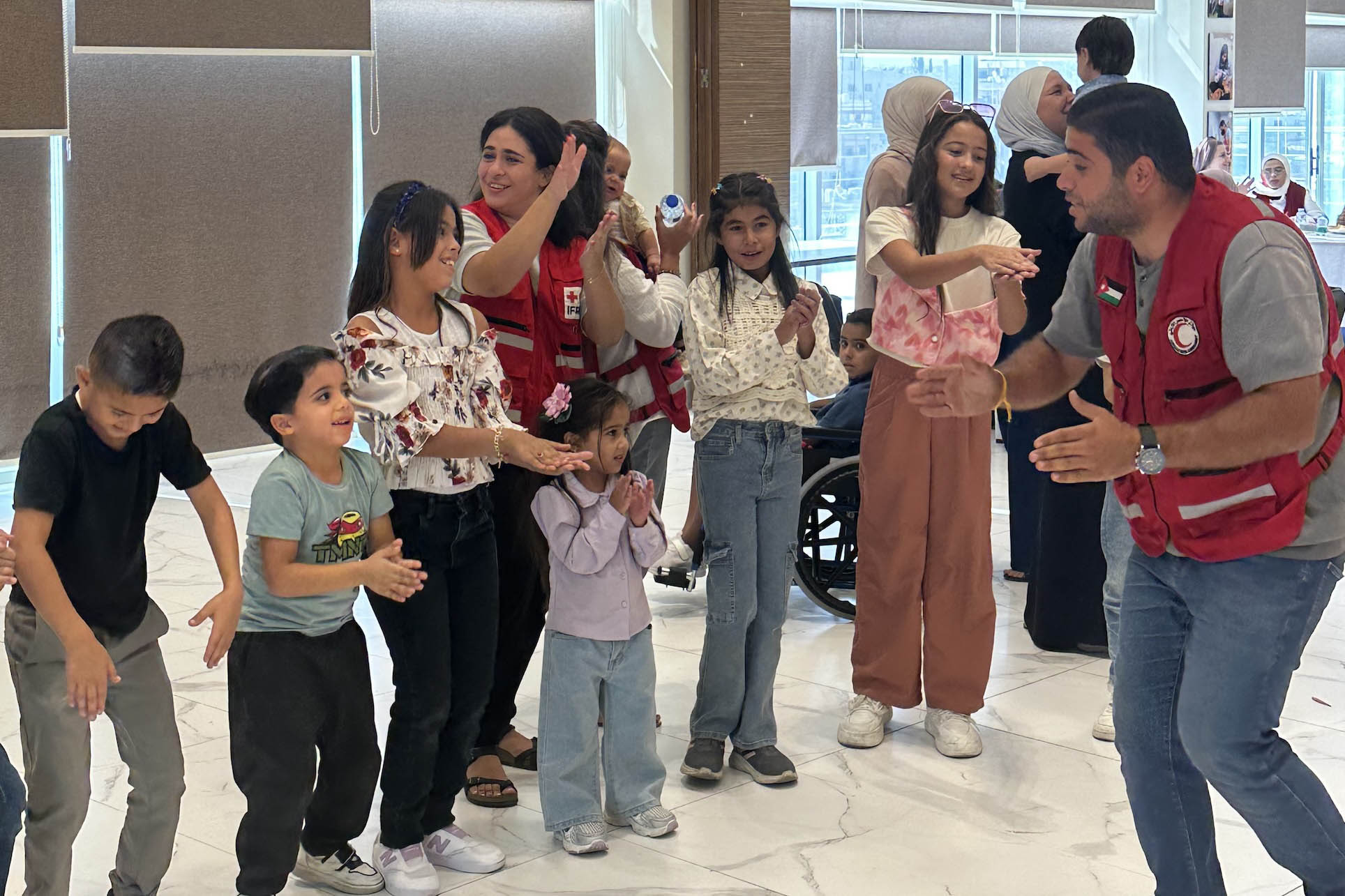 Jordan Red Crescent staff and volunteers lead children in a singing, dancing and clapping game during the birthday celebration of two children who were evacuated from Gaza and are currently receiving care at the hospital.