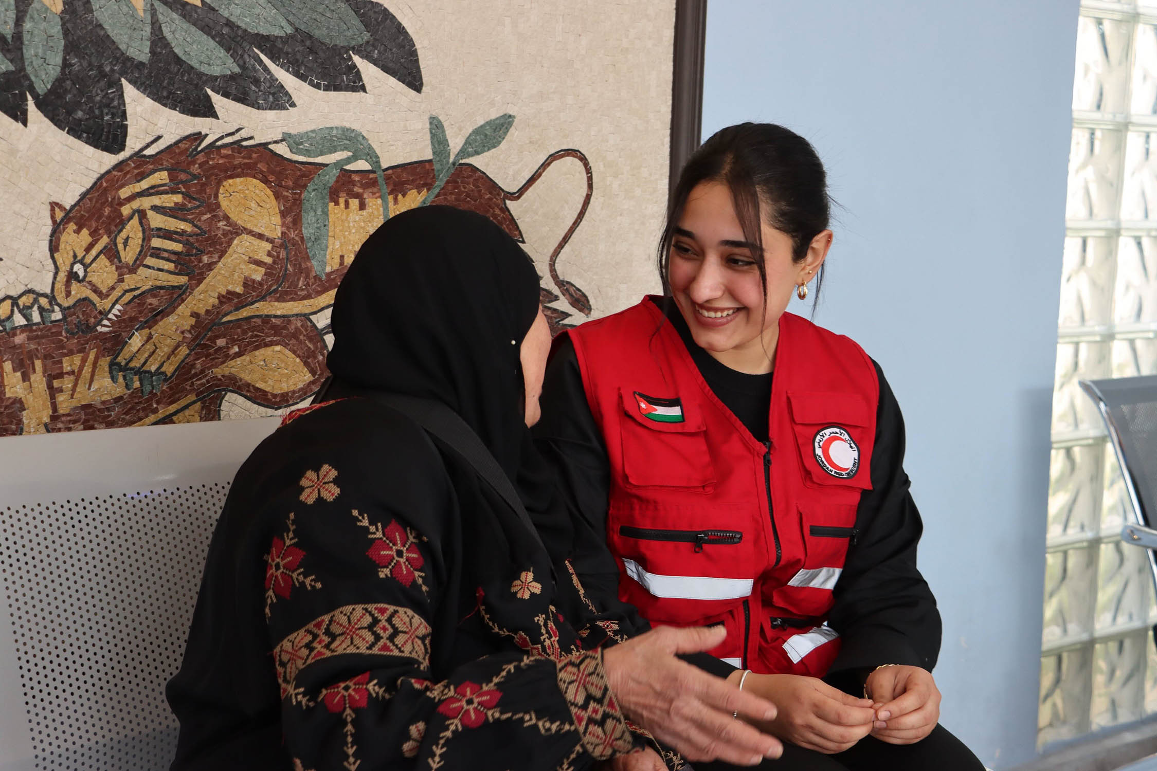 At the Jordan Red Crescent Hospital in Amman, a staff member speaks with an elderly woman who was recently evacuated from Gaza, offering comfort and support after her difficult journey.