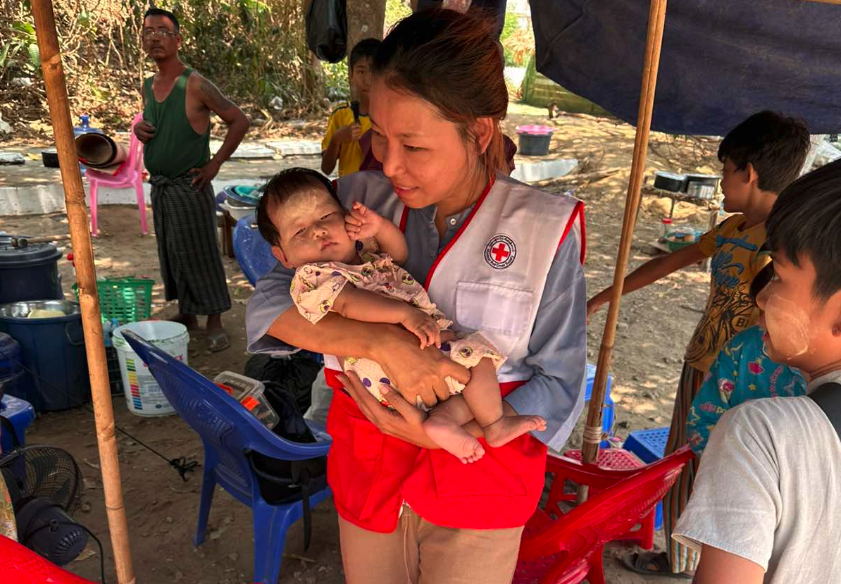 May Tha Gyan holds a baby during a healthcare check in with a family living in a makeshift shelter since the March 28 earthquake.