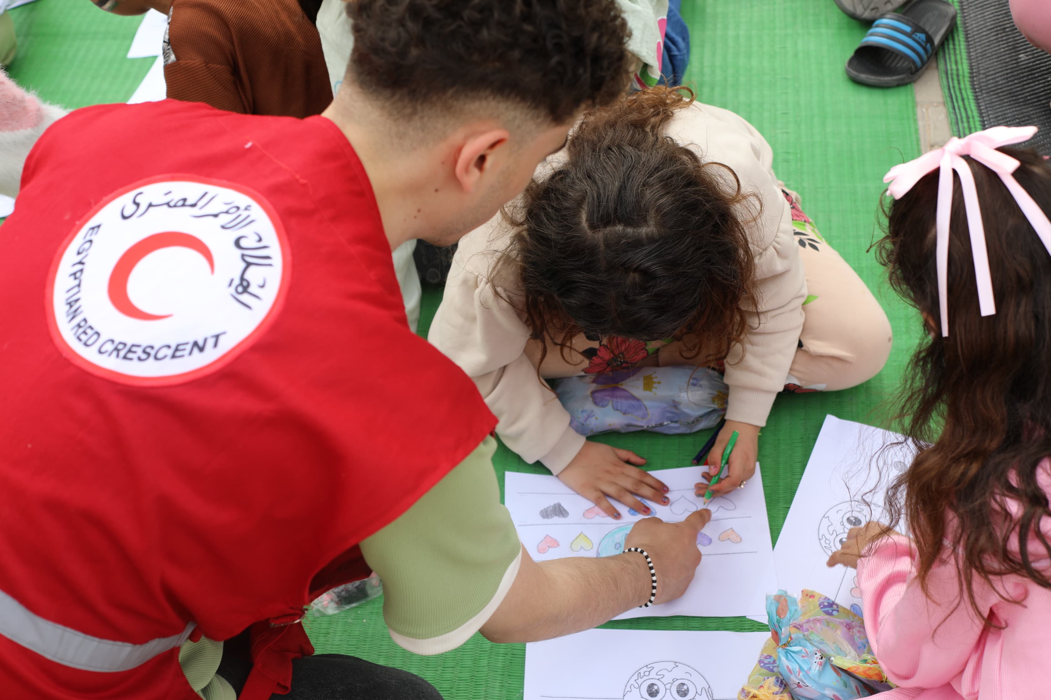 An Egyptian Red Crescent volunteer spending time with children evacuated from Gaza during a drawing activity, part of the wider support offered to evacuee families in Egypt. 