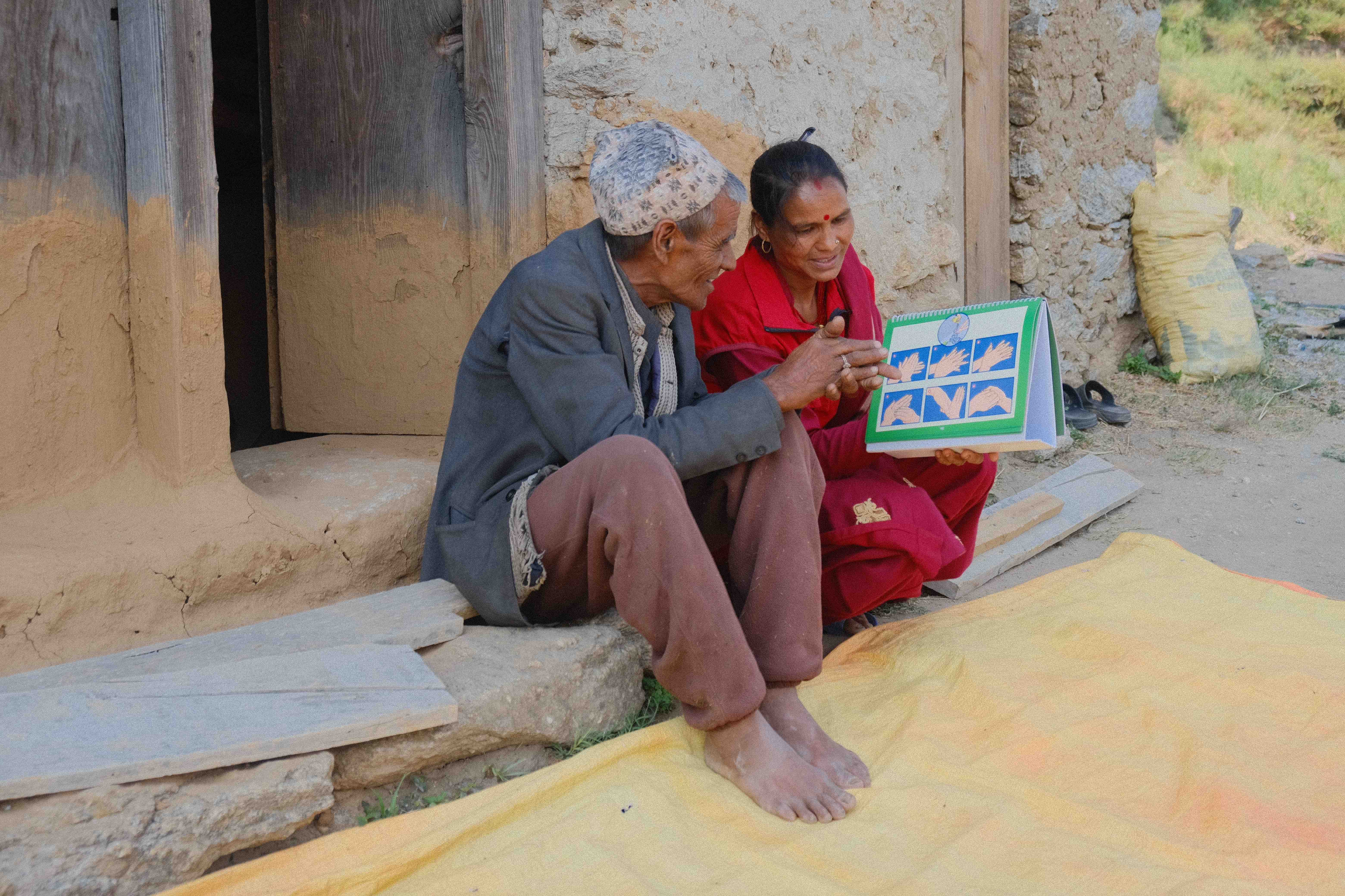 Puri Lal Devkota sits alongside a community health worker who explains how best to wash hands and stay safe from infectious diseases. Puri Lal built a new latrine by himself after the health worker paid him a visit and talked to him about how to improve hygiene practices. 