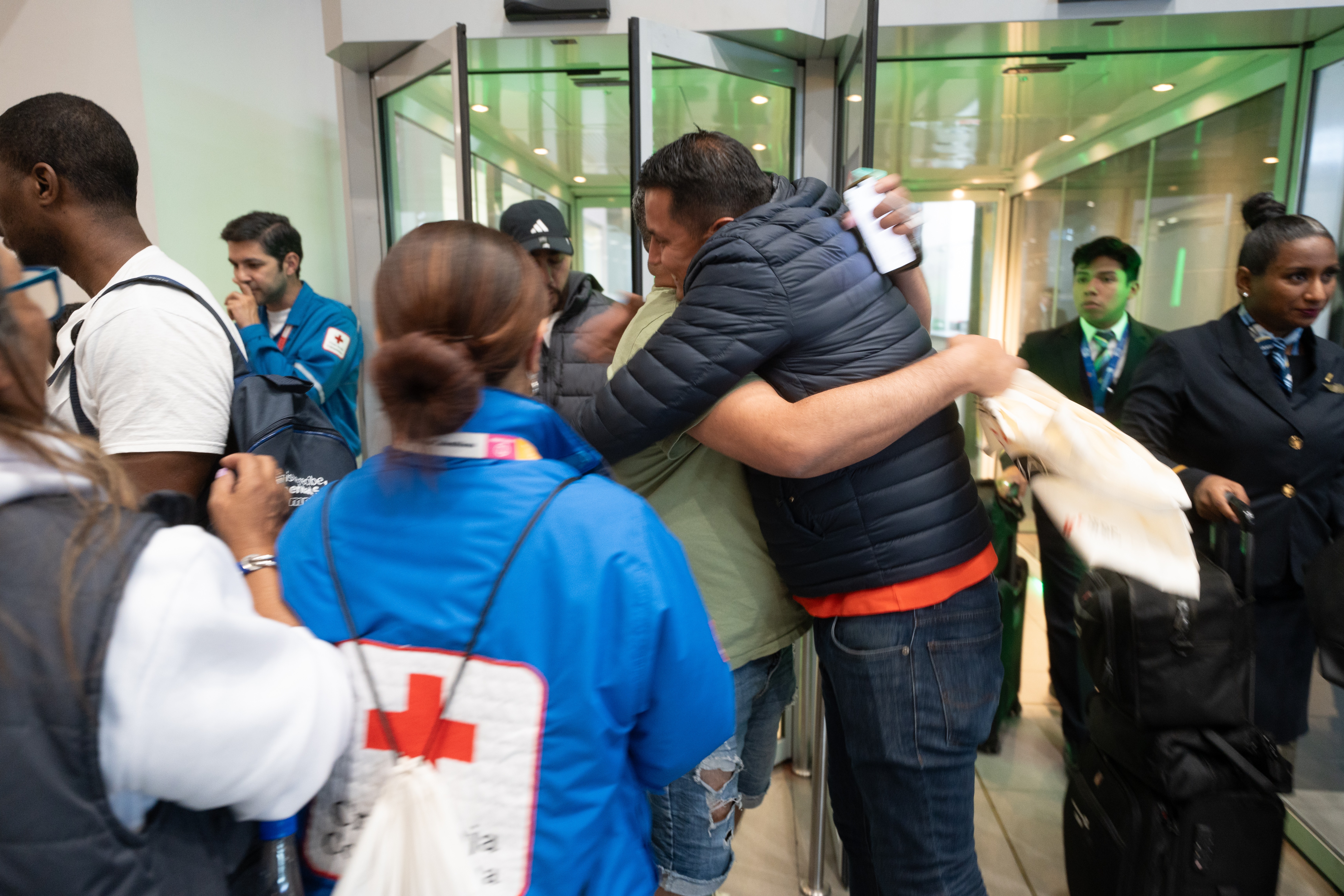 Two men hug each other in the middle of a group of people returning to their country, accompanied by the Colombian Red Cross.