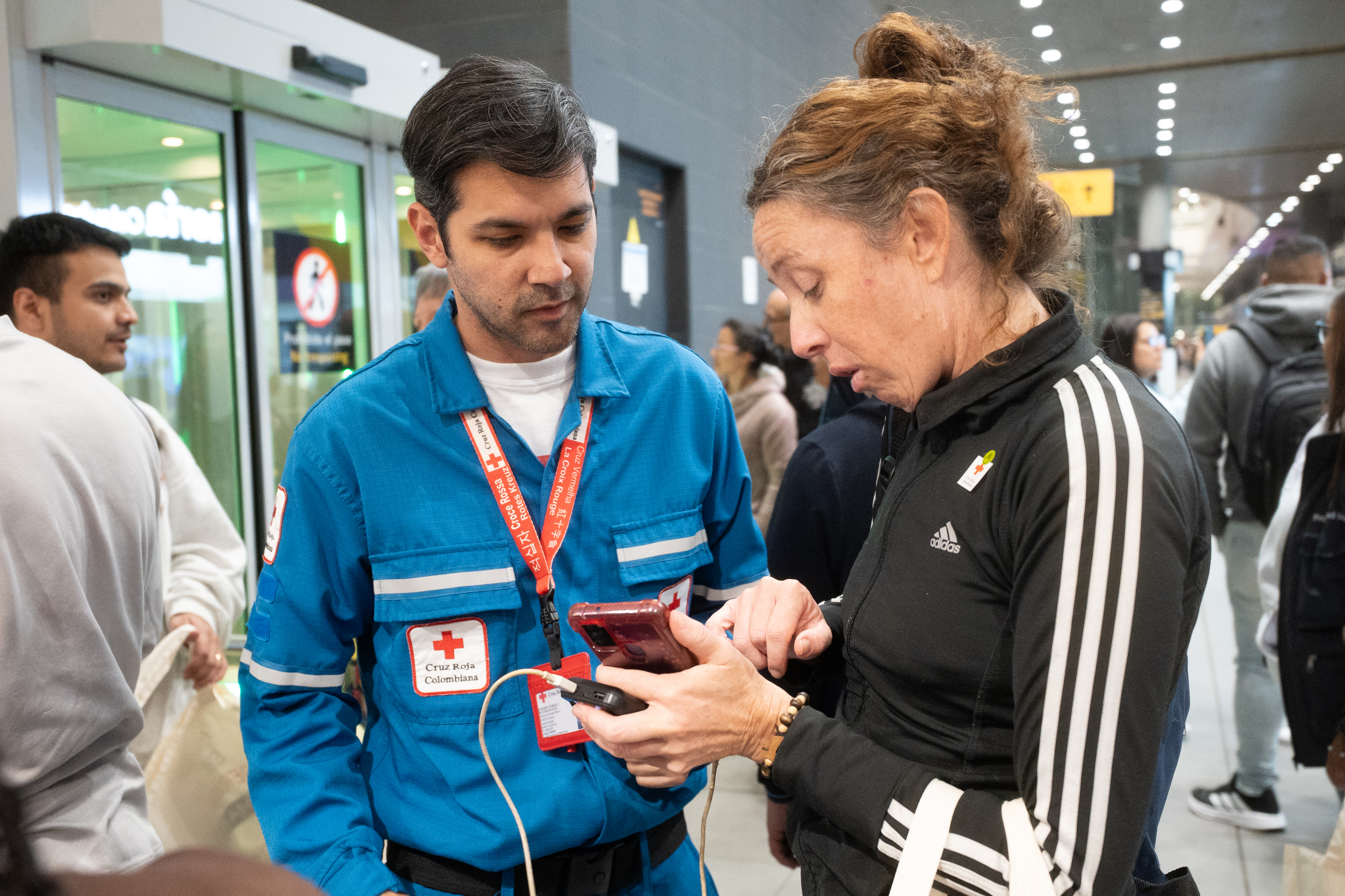 A member of the Colombian Red Cross provides mobile charging and connectivity assistance to a woman who has just returned to Colombia at El Dorado Airport.