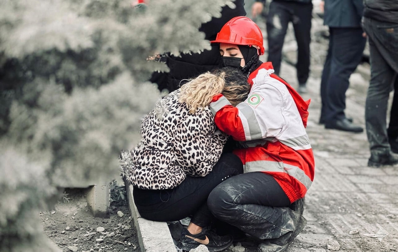 A psychosocial support team member from the Iranian Red Crescent comforts a woman affected by the hostilities, offering emotional support amid ongoing displacement and loss.