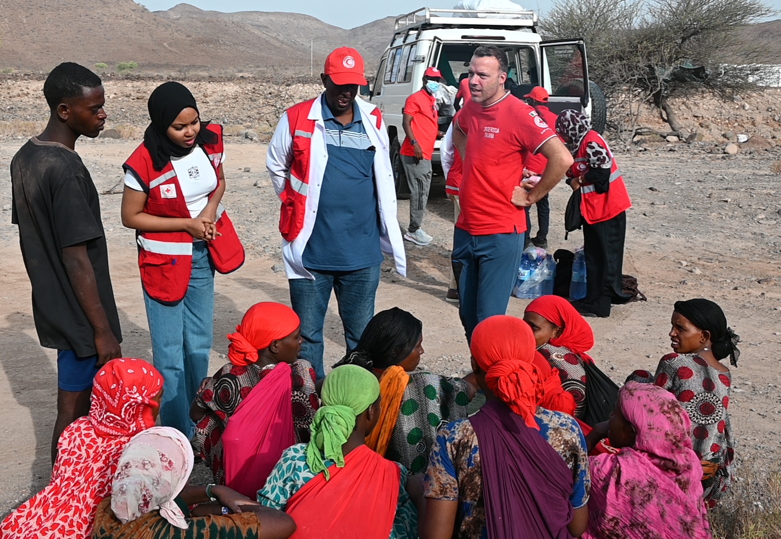 Djibouti Red Crescent staff and volunteers — joined by a representative of the Italian Red Cross — provide food, water, and hygiene items to a group of people walking through a  precarious and remote stretch of roadway. 
