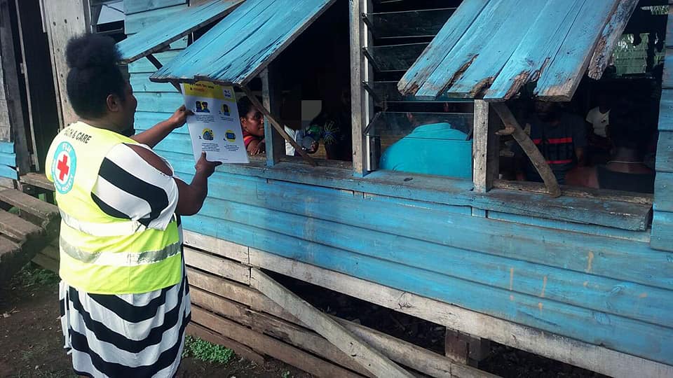 Taraivini Kabuta, Fiji Red Cross volunteer shares a message about COVID-19 transmissions through a window to a family in Uciwai Settlement, Fiji.