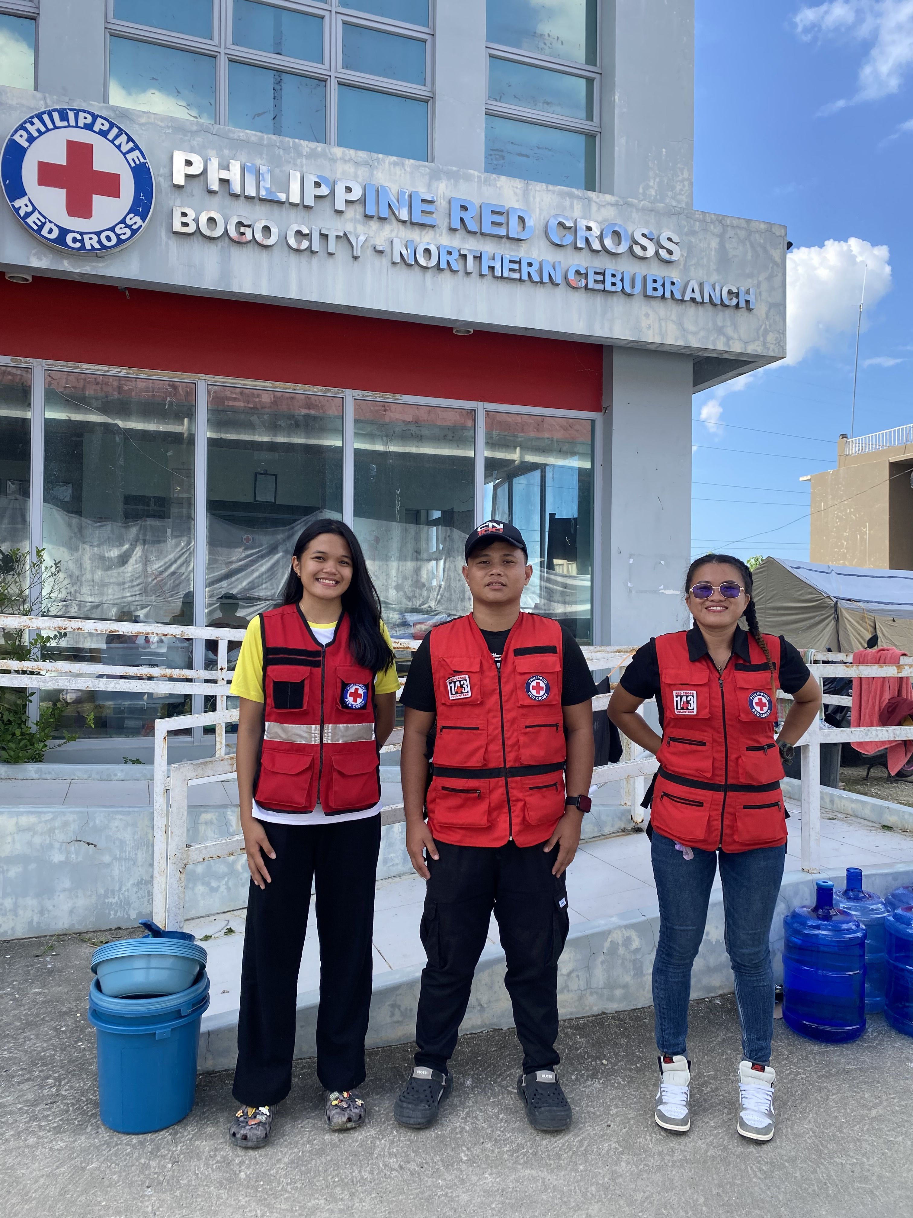 Philippine Red Cross volunteers (L-R) Marea Noelle Magnanao, Margien Baterna and Algon Gomez in front of the Bogo City Red Cross branch building, which had been damaged in the quake. Photo: Ellie van Baaren/IFRC