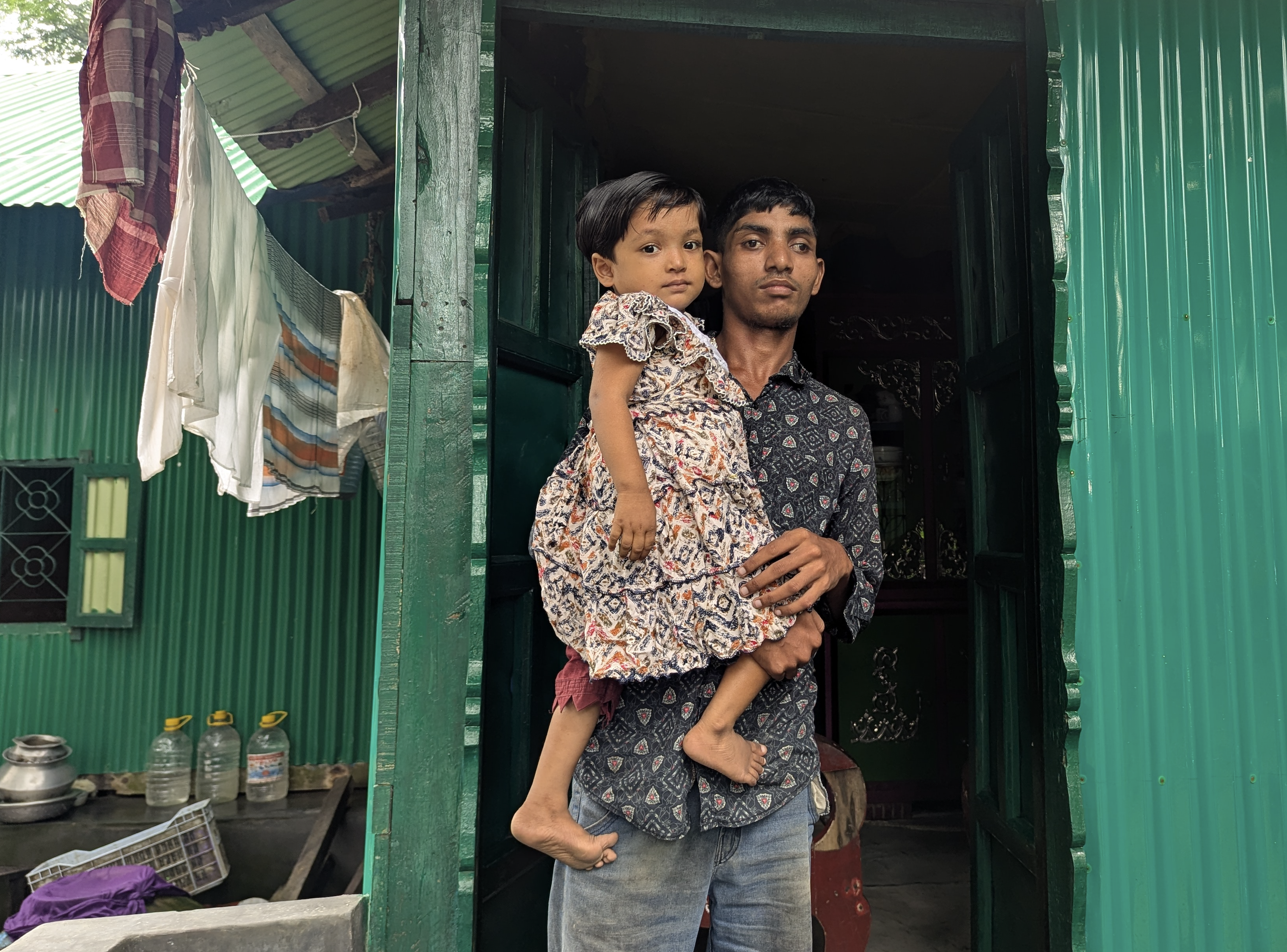Ismail holds his daughter as he stands in the doorway of his new home, built with support from the IFRC emergency appeal. Photo: Bangladesh Red Crescent 