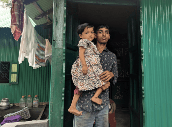 Ismail holds his daughter as he stands in the doorway of his new home, built with support from the IFRC emergency appeal. Photo: Bangladesh Red Crescent 