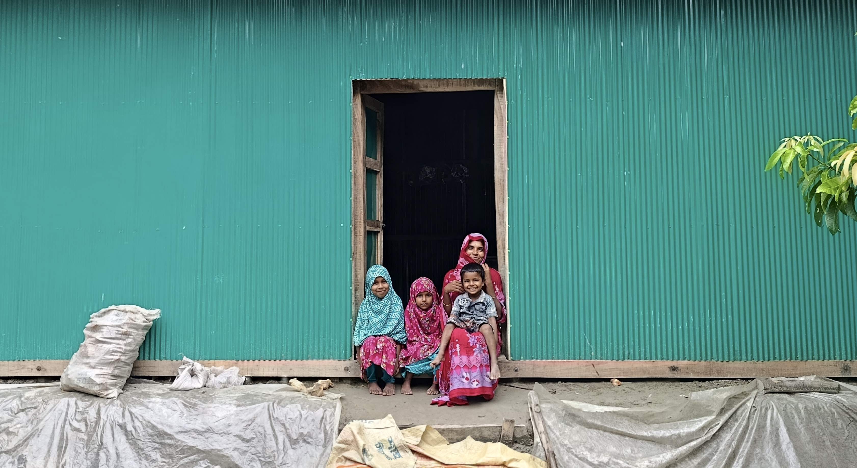 Noyon Akter sits with her children in front of her new shelter, provided with support from an IFRC emergency appeal. Photo: Bangladesh Red Crescent Society