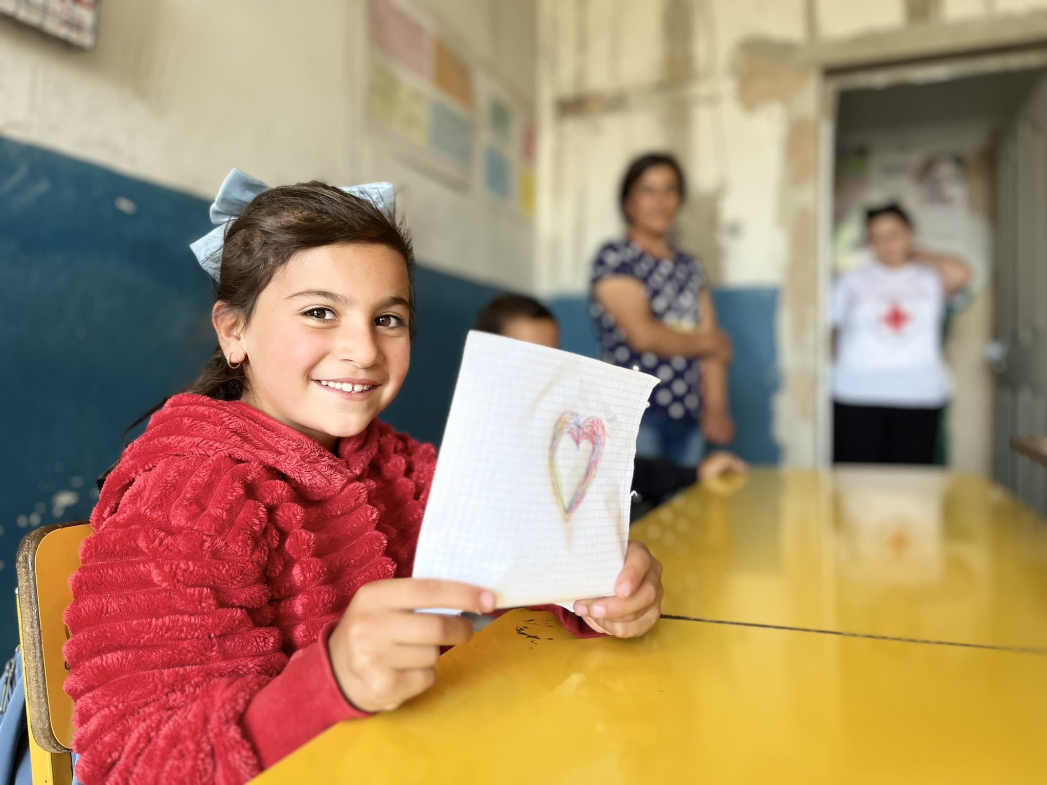 Une fillette brandit un dessin représentant un cœur dans une école qui a reçu l'aide de la Croix-Rouge arménienne.