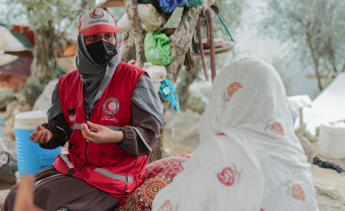 Afghan Red Crescent volunteer Sharifa visits with a woman and consults on health care needs following a 6.0 magnitude earthquake in August 2025.