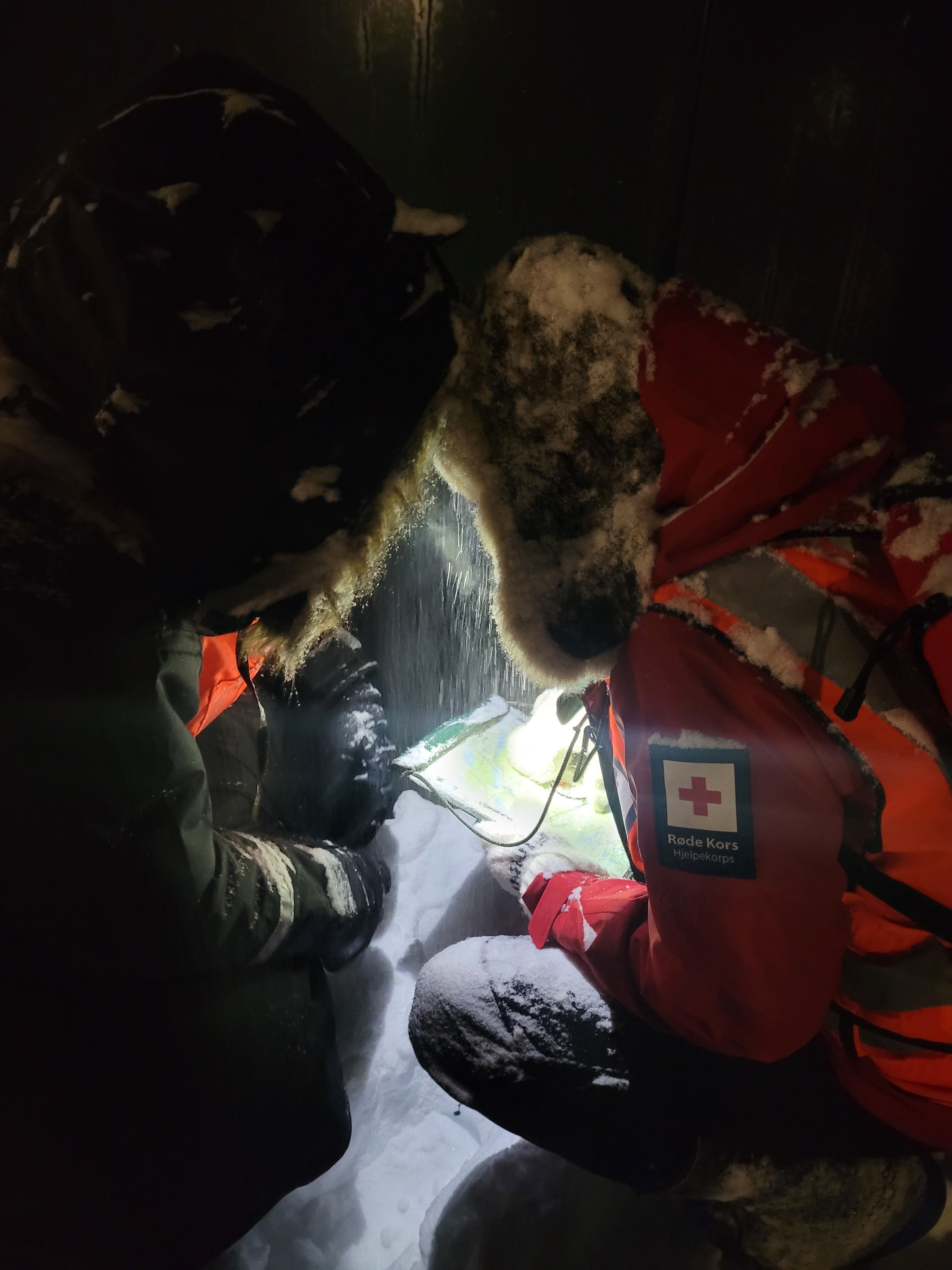Volunteers for the Norwegian Red Cross use headlamps to check their maps in a snowstorm.