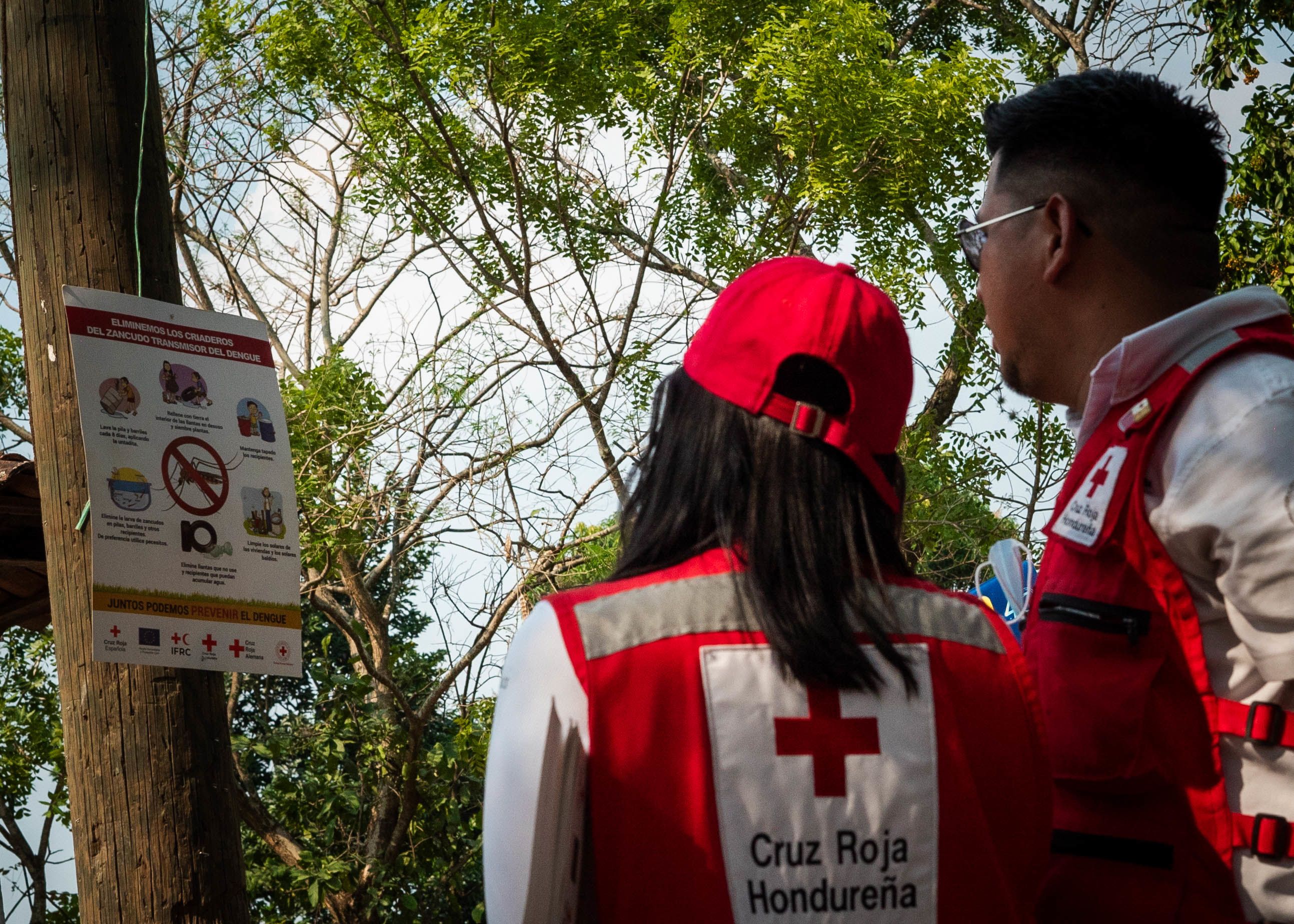 un voluntario y una voluntaria de Cruz Roja Hondureña instalan un cartel de prevención de riesgos