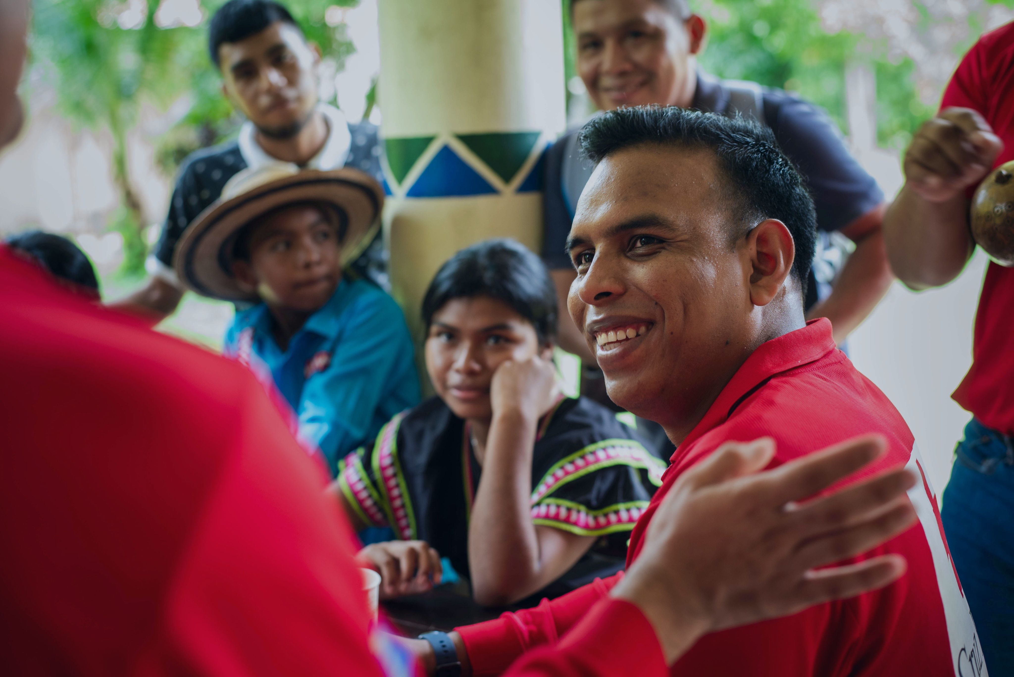 Un voluntario de Cruz Roja Panameña sonríe mientras otra persona, a la que solo le vemos su mano, le da una palmada en la espalda. Detrás de él vemos a personas indígenas de Chiriquí