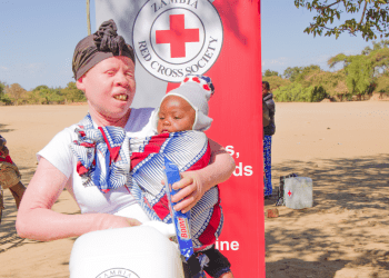 Muleya Sikuteka holds her baby and a 20-litre water container received during a Zambia Red Cross hygiene kit distribution in Sinazongwe.