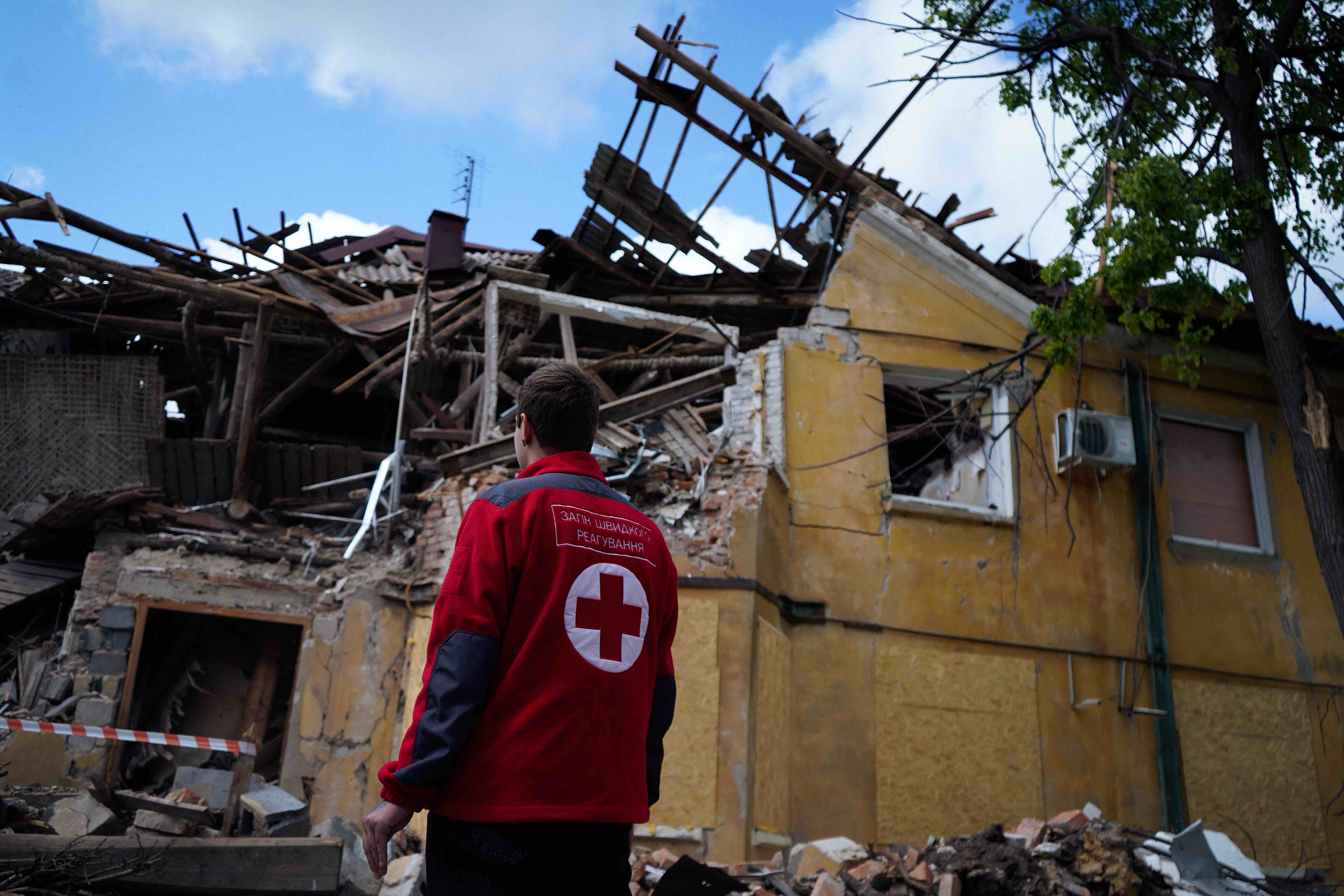 A Ukrainian Red Cross volunteer stands outside a home destroyed by bombing.